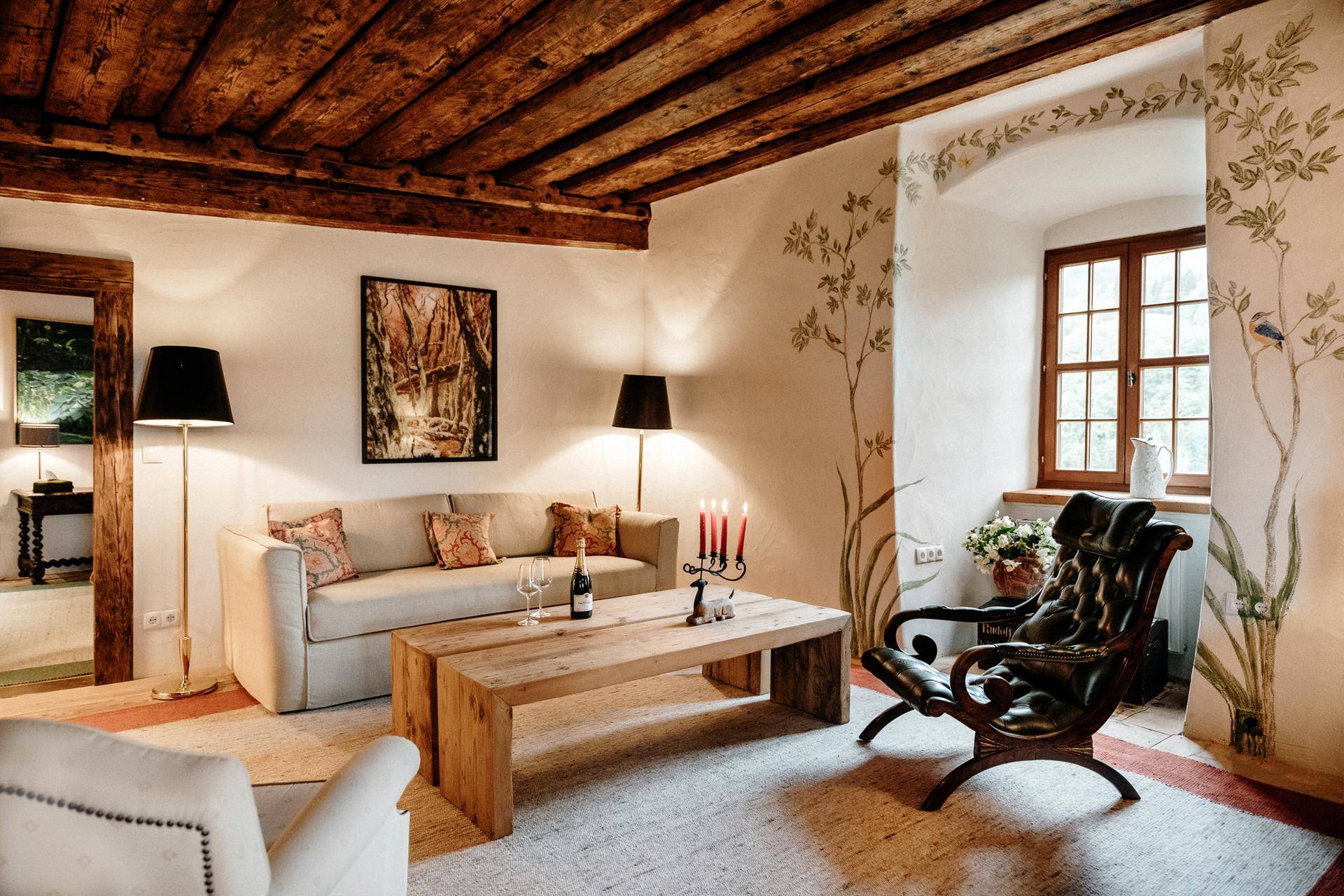 Helles Wohnzimmer mit Holzbalkendecke, Holztisch und dekorativen Wandmalereien.