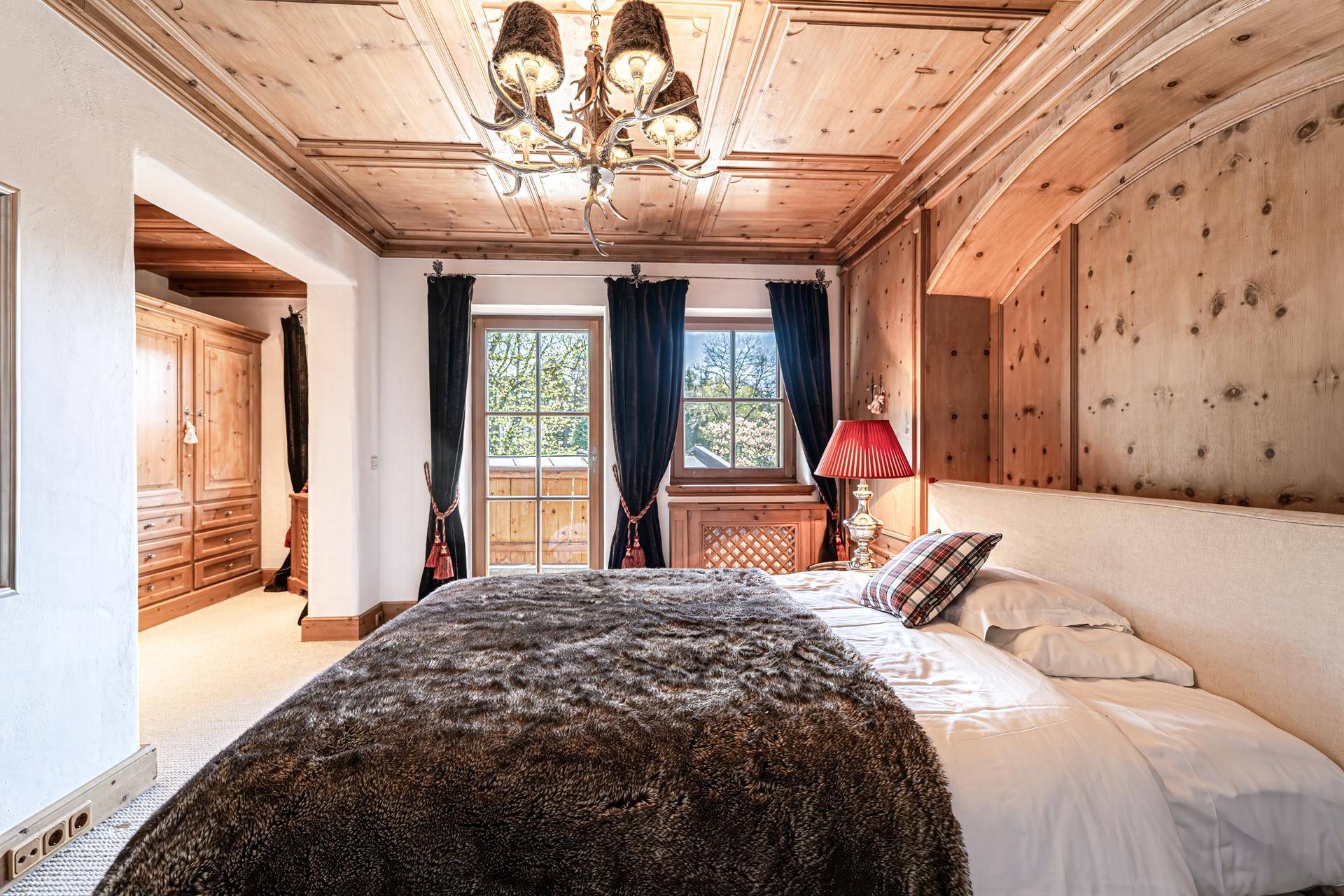 Gemütliches Schlafzimmer im alpinen Stil mit Holzwänden, Holzbalkendecke und Zugang zum Balkon.