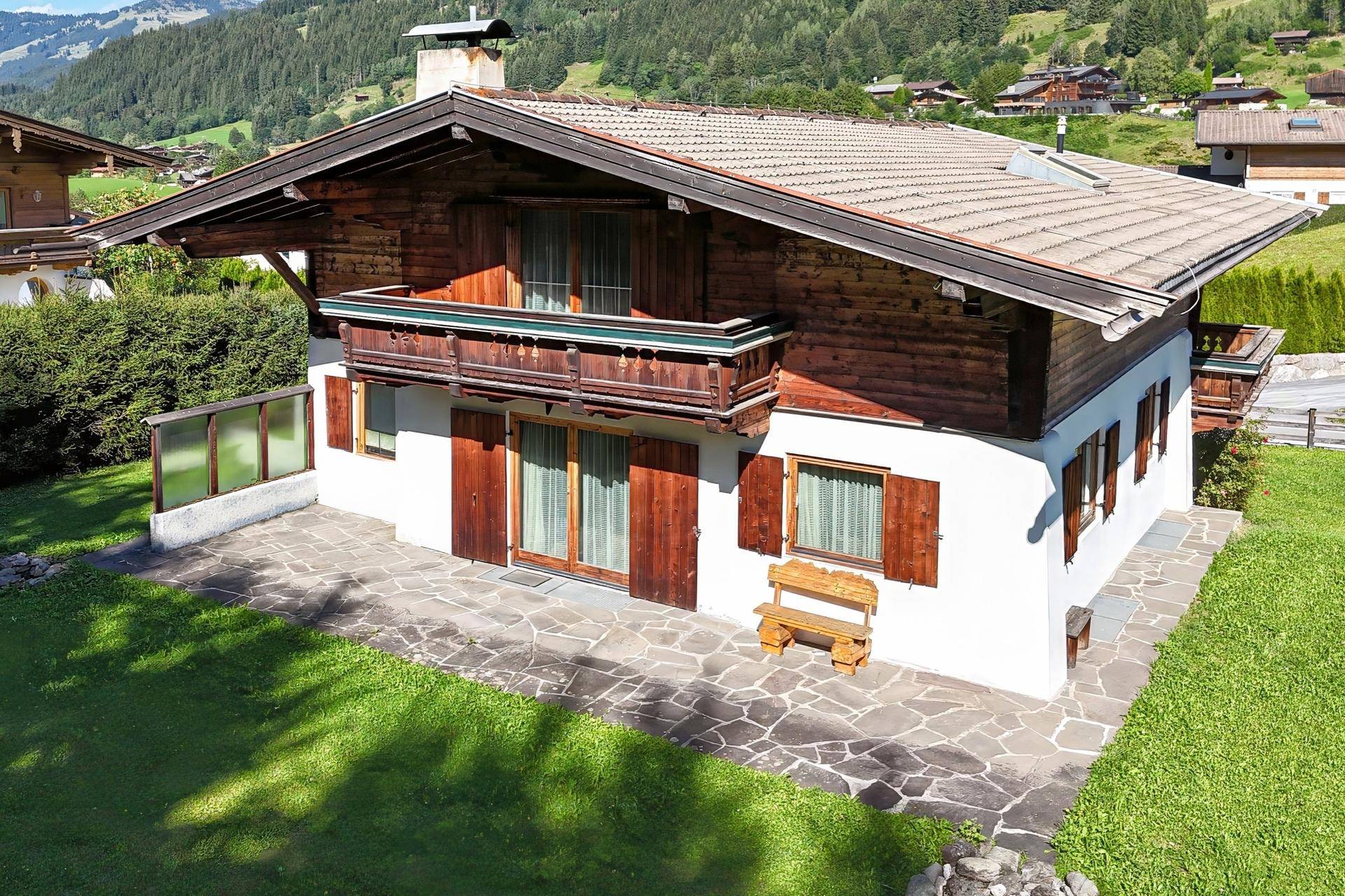 Charmantes Haus mit Steinterrasse und gepflegtem Rasen, umgeben von grüner Natur und Bergen.