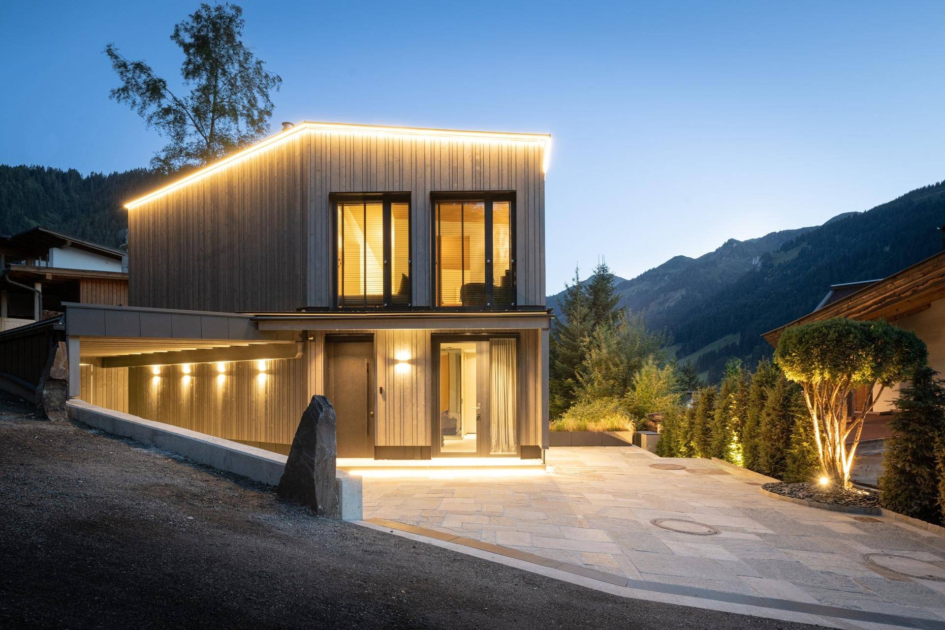 Zeitgenössisches Haus mit Holzfassade und Carport, eingebettet in die Berglandschaft.