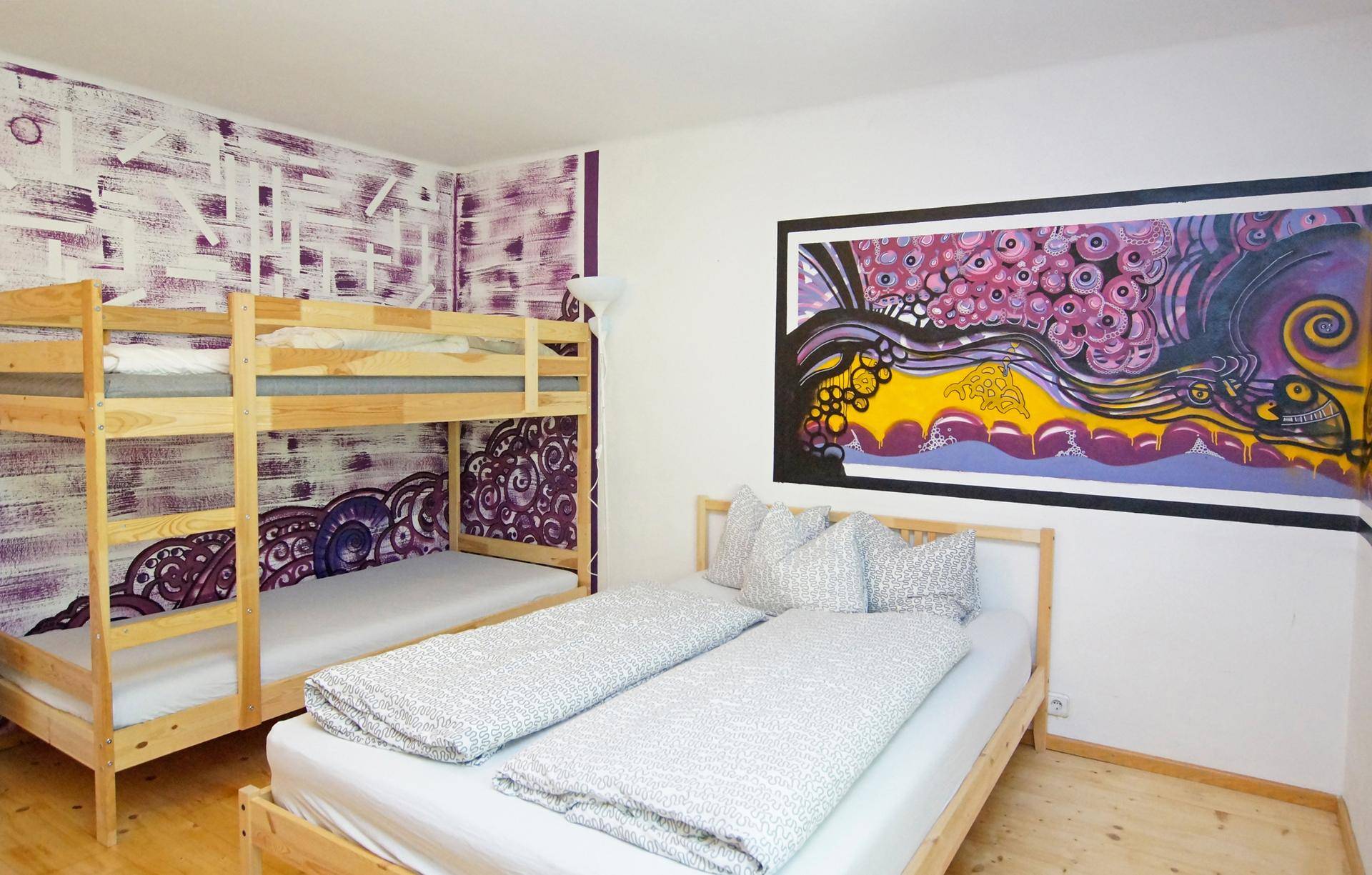 Geräumiges Schlafzimmer mit Doppelbett, Etagenbett und kreativer Wandkunst in Lila- und Gelbtönen.
