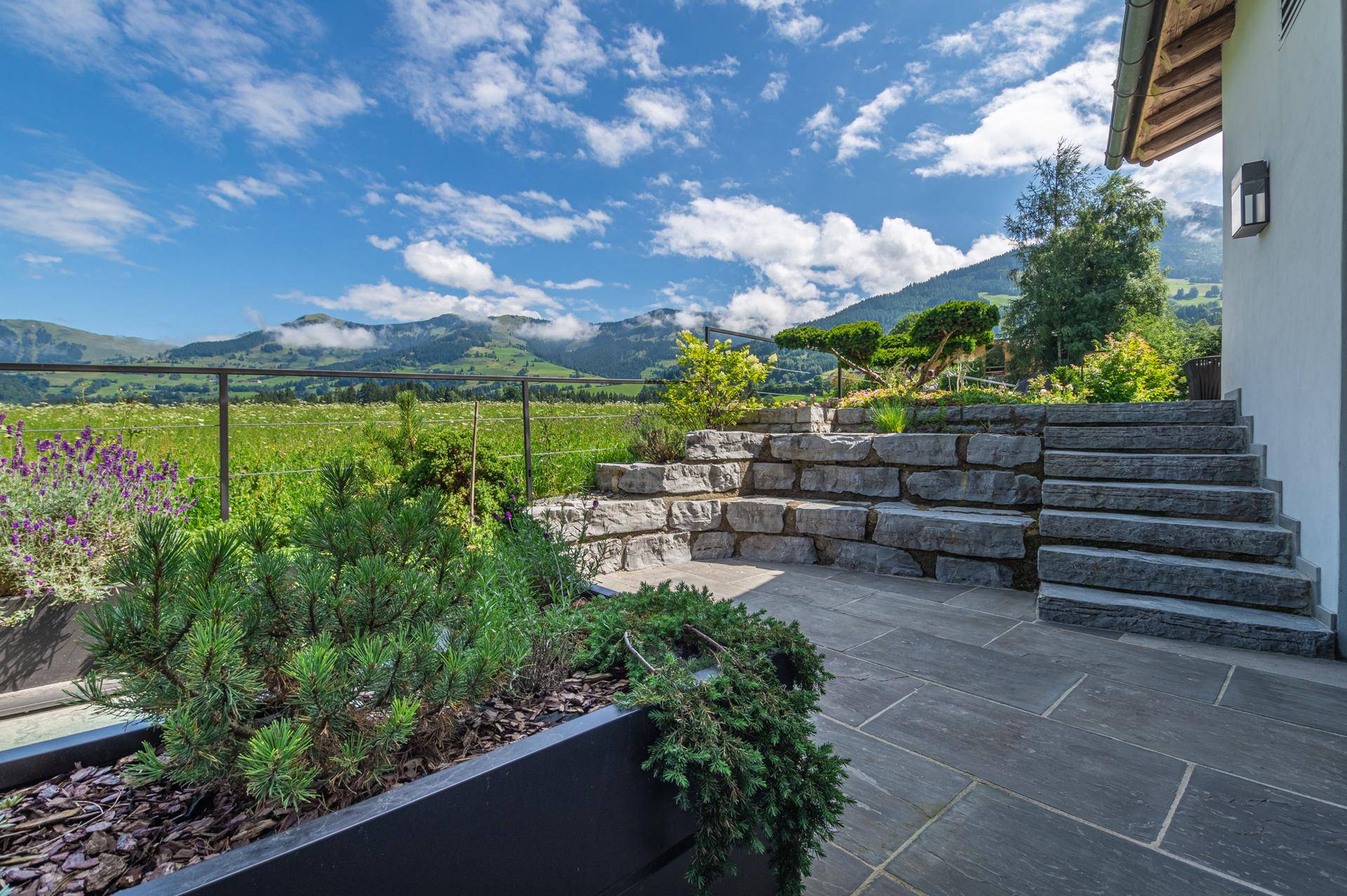 Gepflegter Gartenbereich mit Steintreppen, Pflanzen und weitem Bergblick.