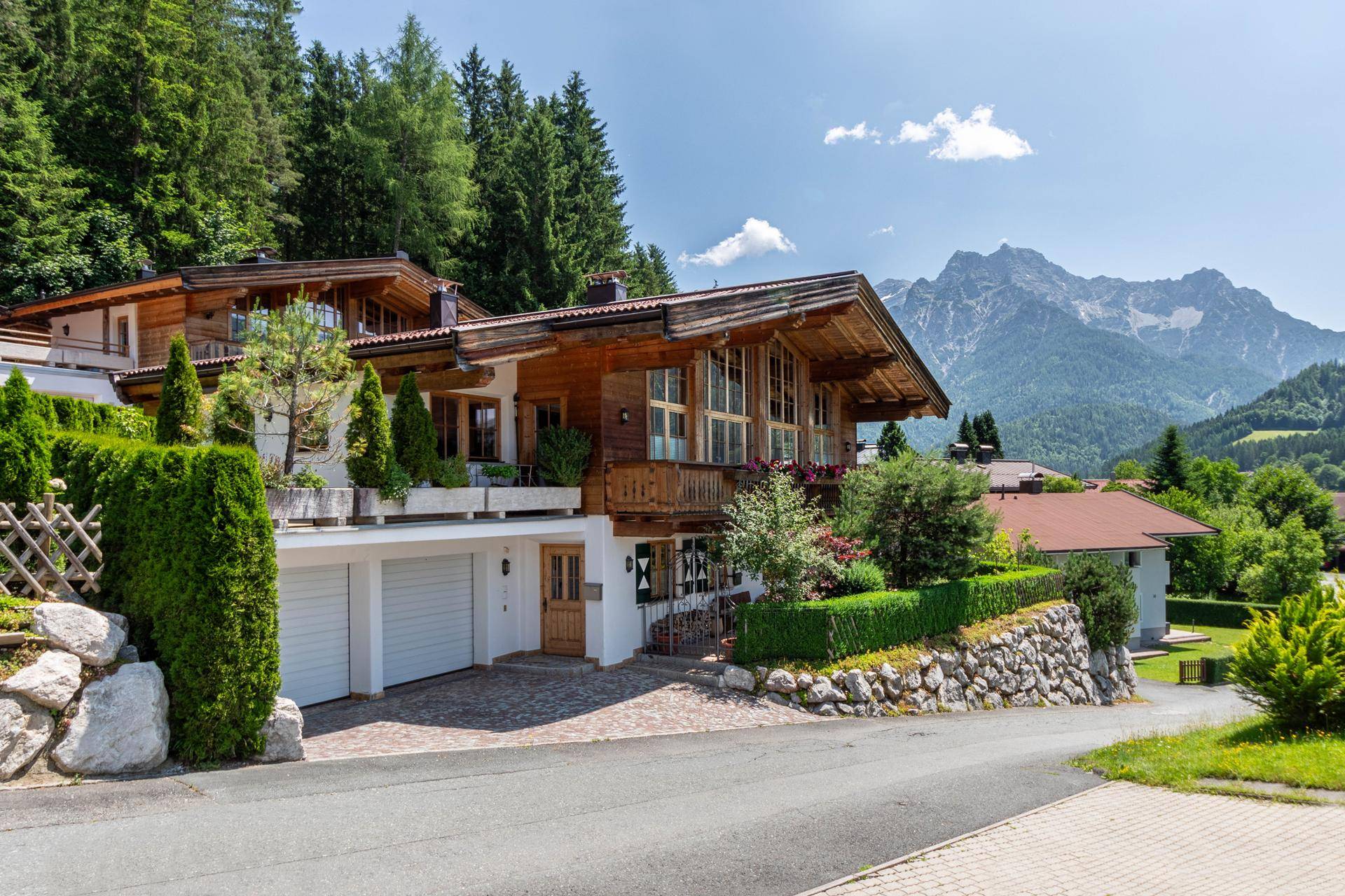 Traditionelles Holzhaus im alpinen Stil mit Doppelgarage und Bergblick, umgeben von viel Grün.
