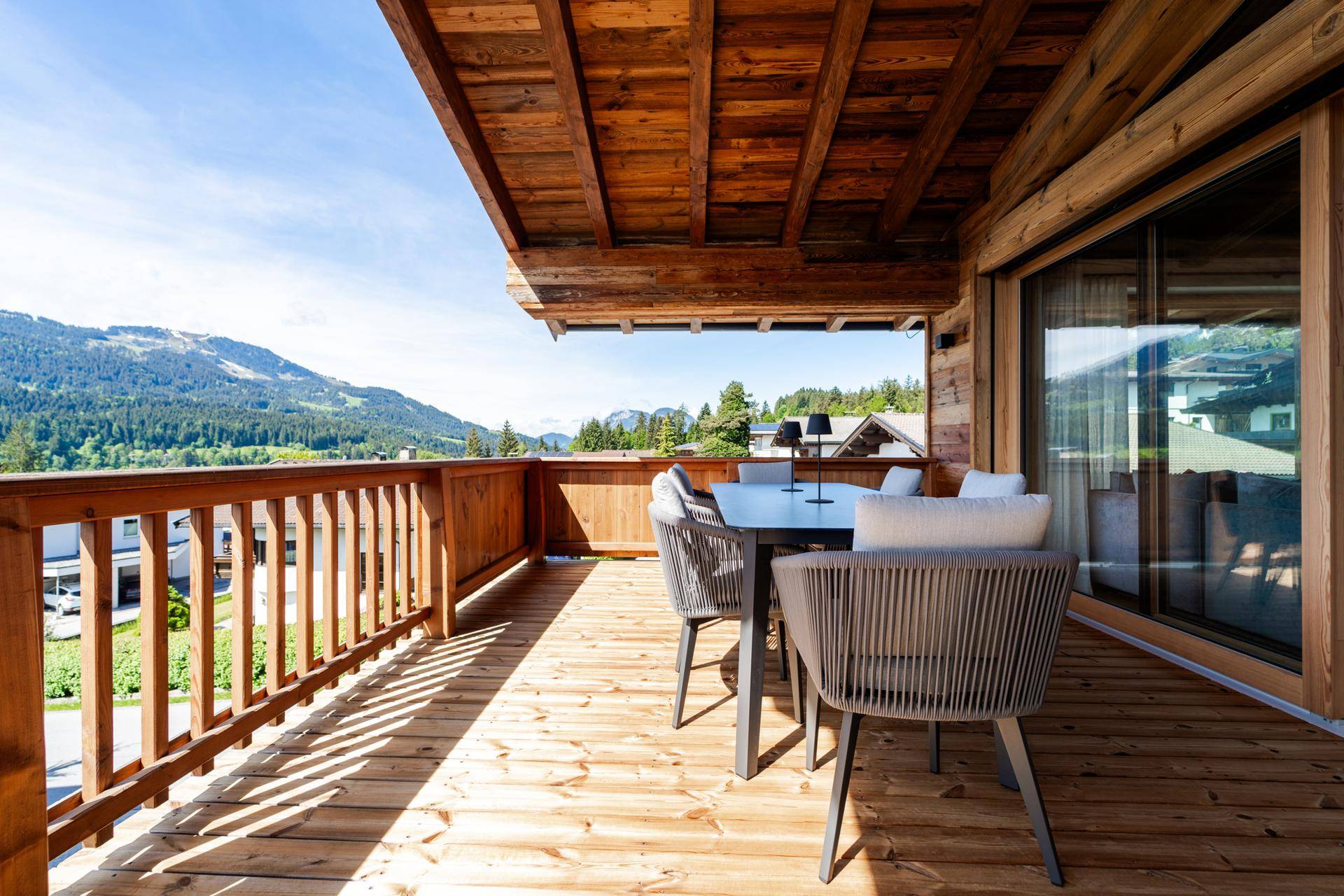 Geräumiger Holzbalkon mit bequemen Gartenmöbeln und weitem Blick auf die umliegende Berglandschaft.