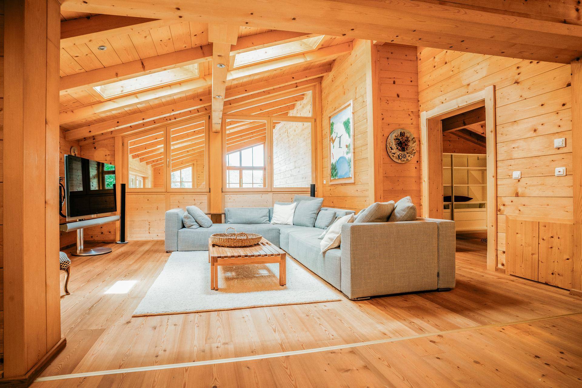 Geräumiges Wohnzimmer im Chalet-Stil mit Holzböden, Holzwänden, Dachschrägen und großen Fenstern.