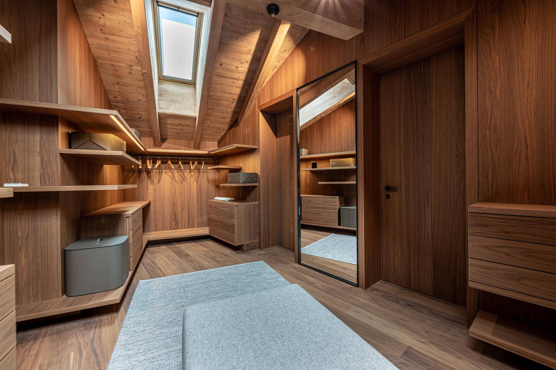 Geräumiger begehbarer Kleiderschrank mit Holzregalen, Spiegel und Dachfenster.