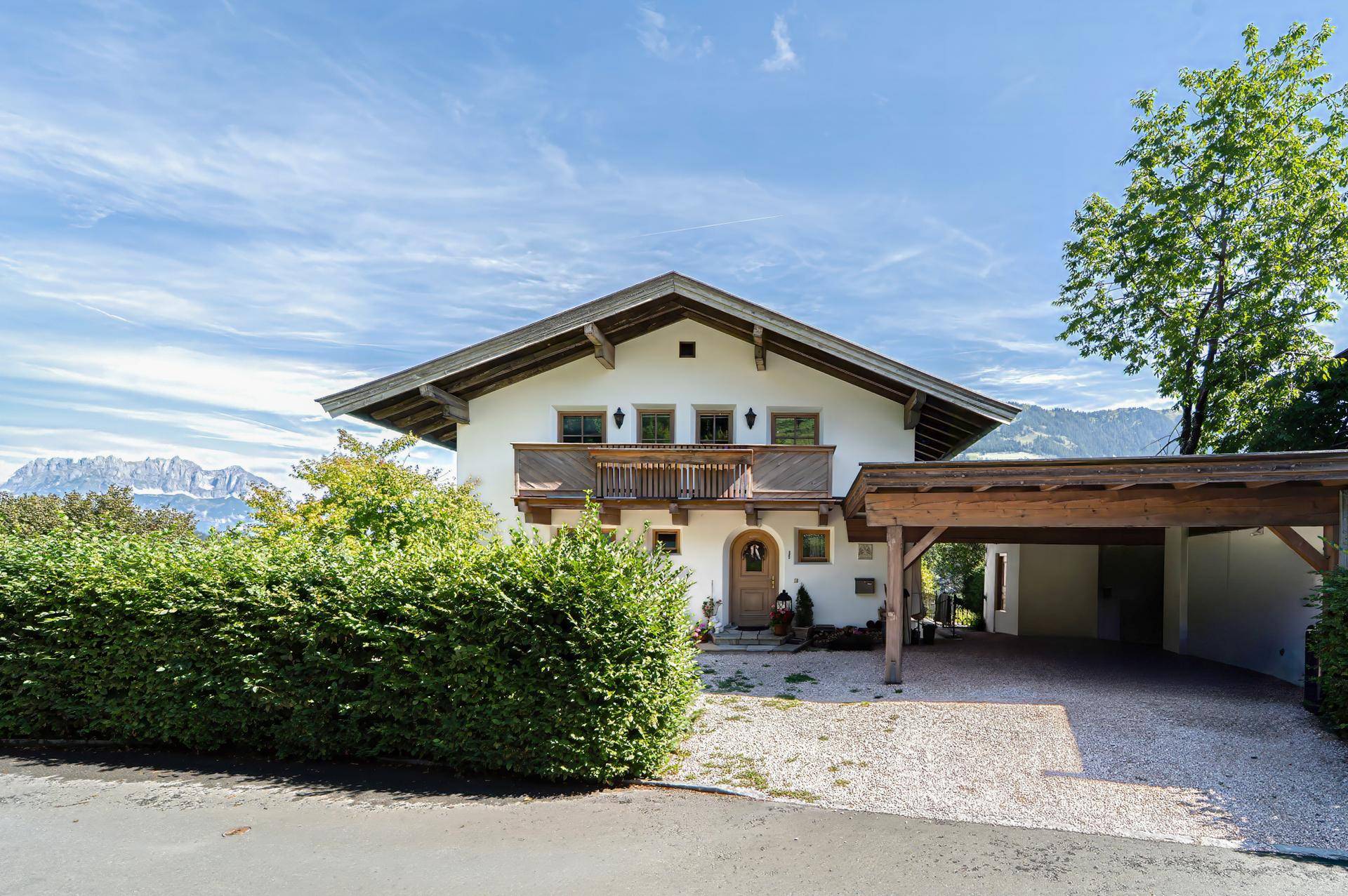 Traditionelles Haus mit Satteldach, Holzbalkon und einem Carport im Vorgarten.