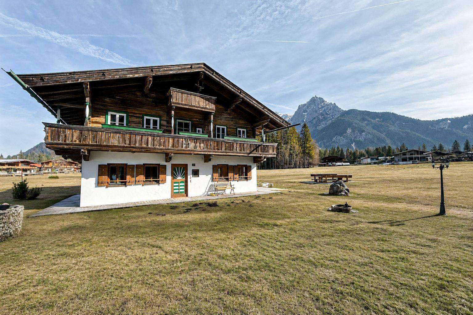 Charmantes Holzhaus im Alpenstil mit Balkon und Blick auf die umliegende Bergwelt und weite Wiesen.