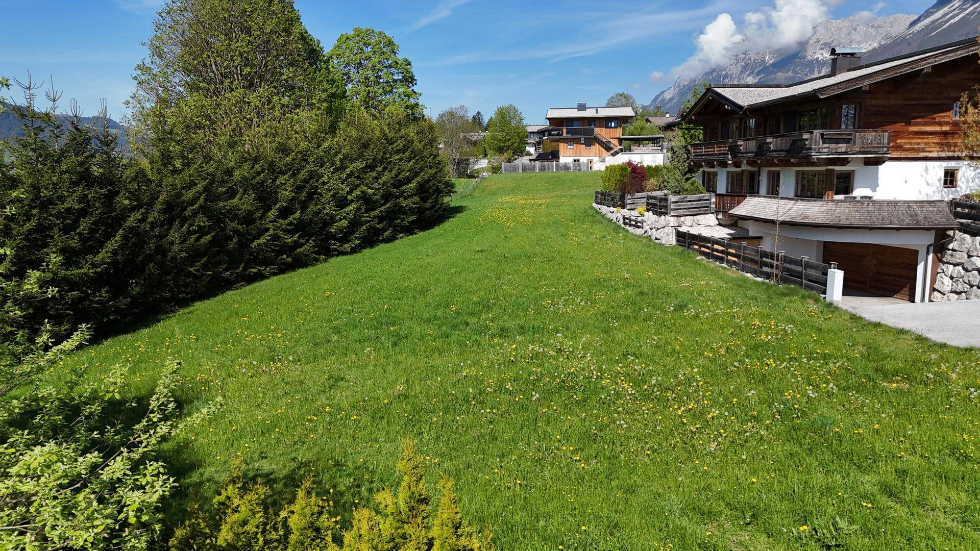 Grüne Wiese neben dem Haus mit Bäumen und Blick auf die umliegende Berglandschaft.