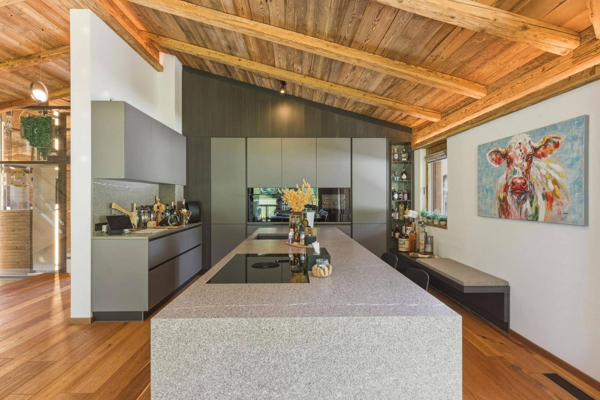 Moderne Küche mit grauen Schränken, großer Kochinsel und Holzbalkendecke.