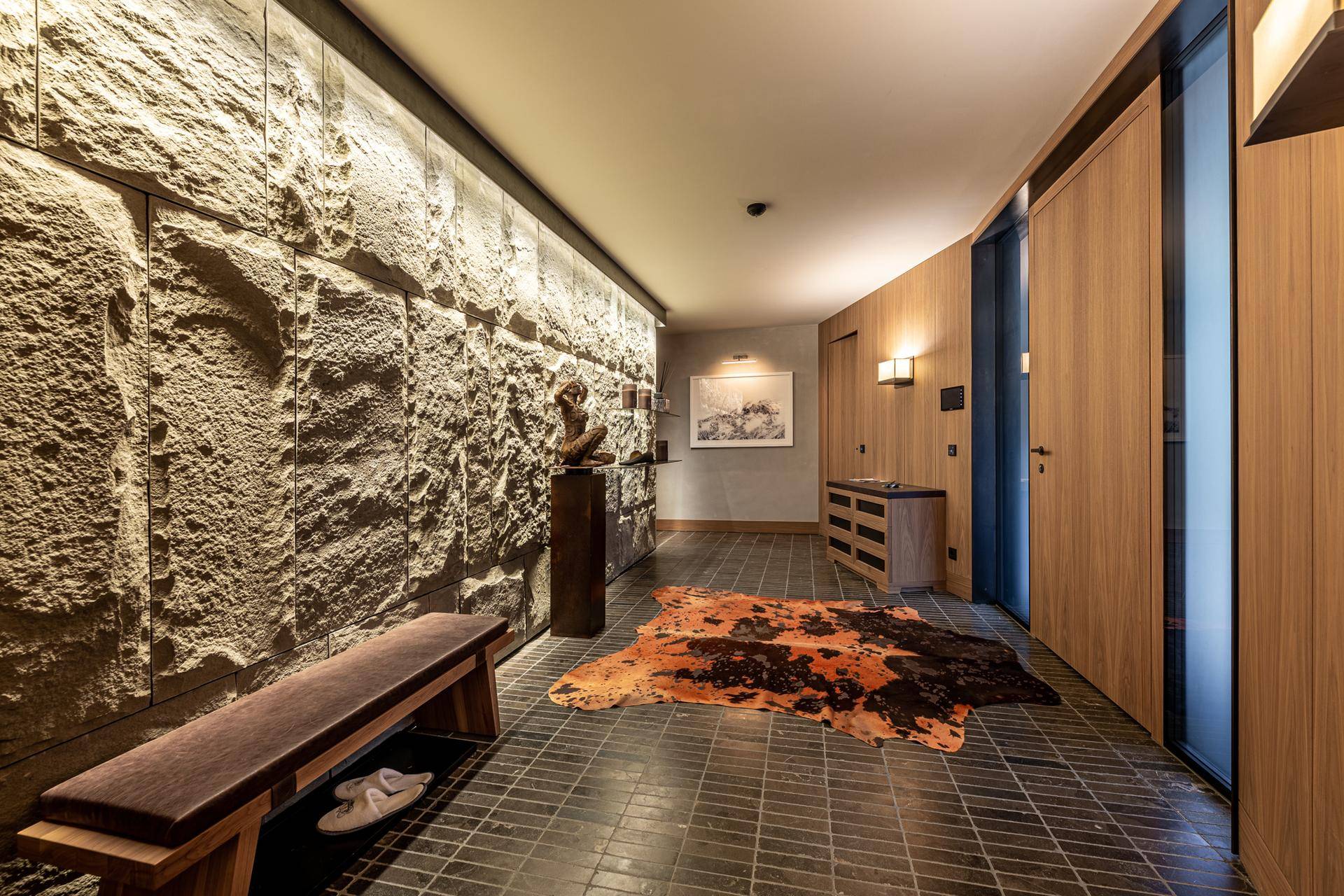 Moderner Flur mit Steinwand, Holzelementen und dekorativem Teppich.