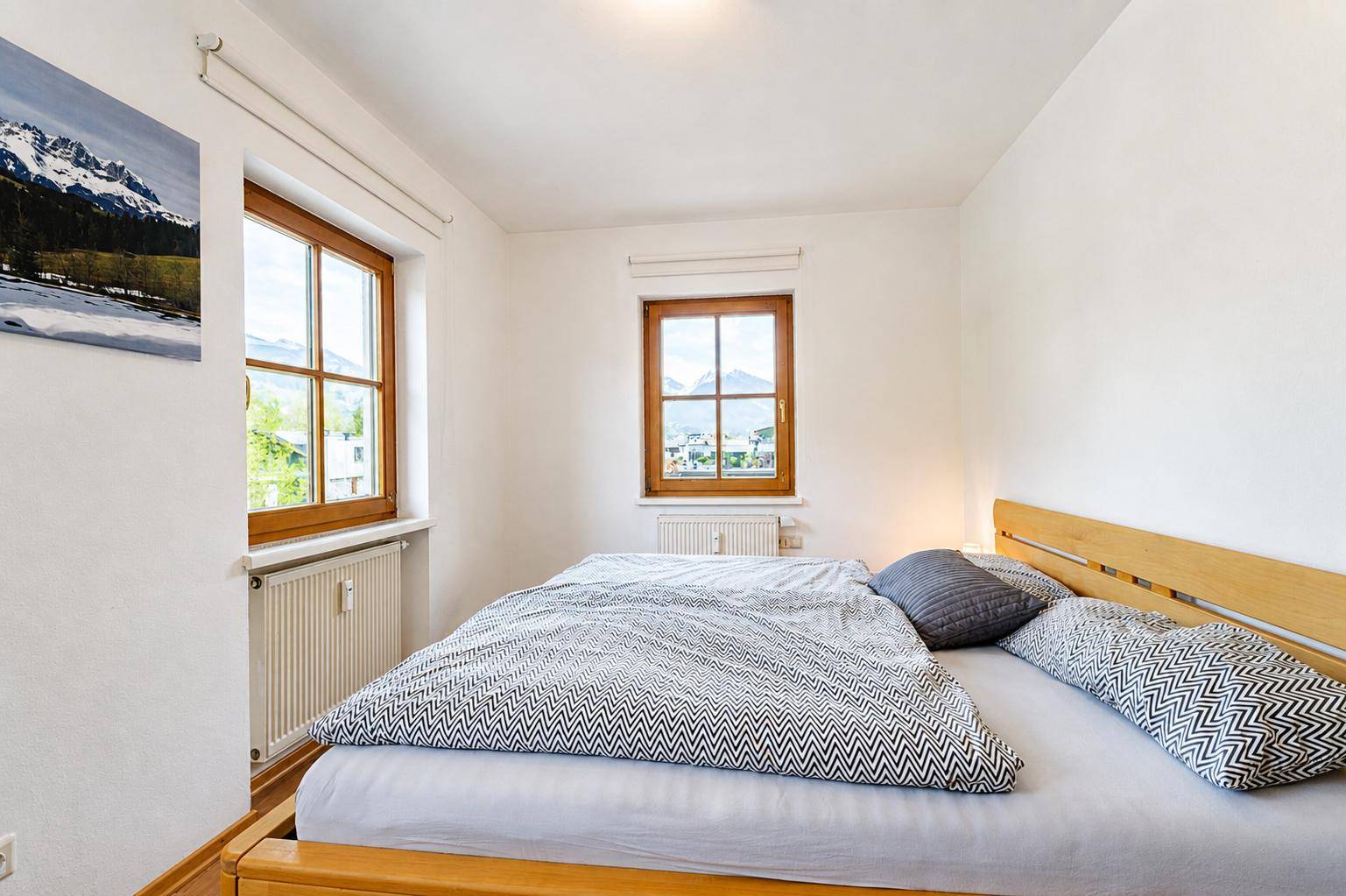 Helles Schlafzimmer mit Holzbett und malerischem Bergblick durch die Fenster.
