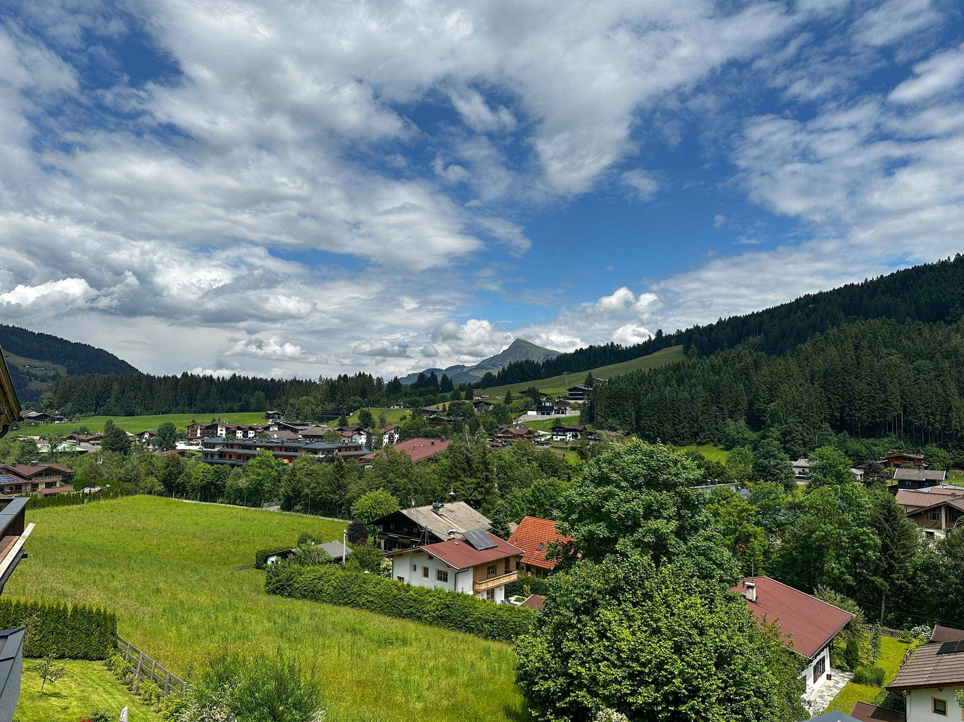 Weitläufiger Blick auf die grüne Berglandschaft und die umliegenden Häuser unter blauem Himmel.