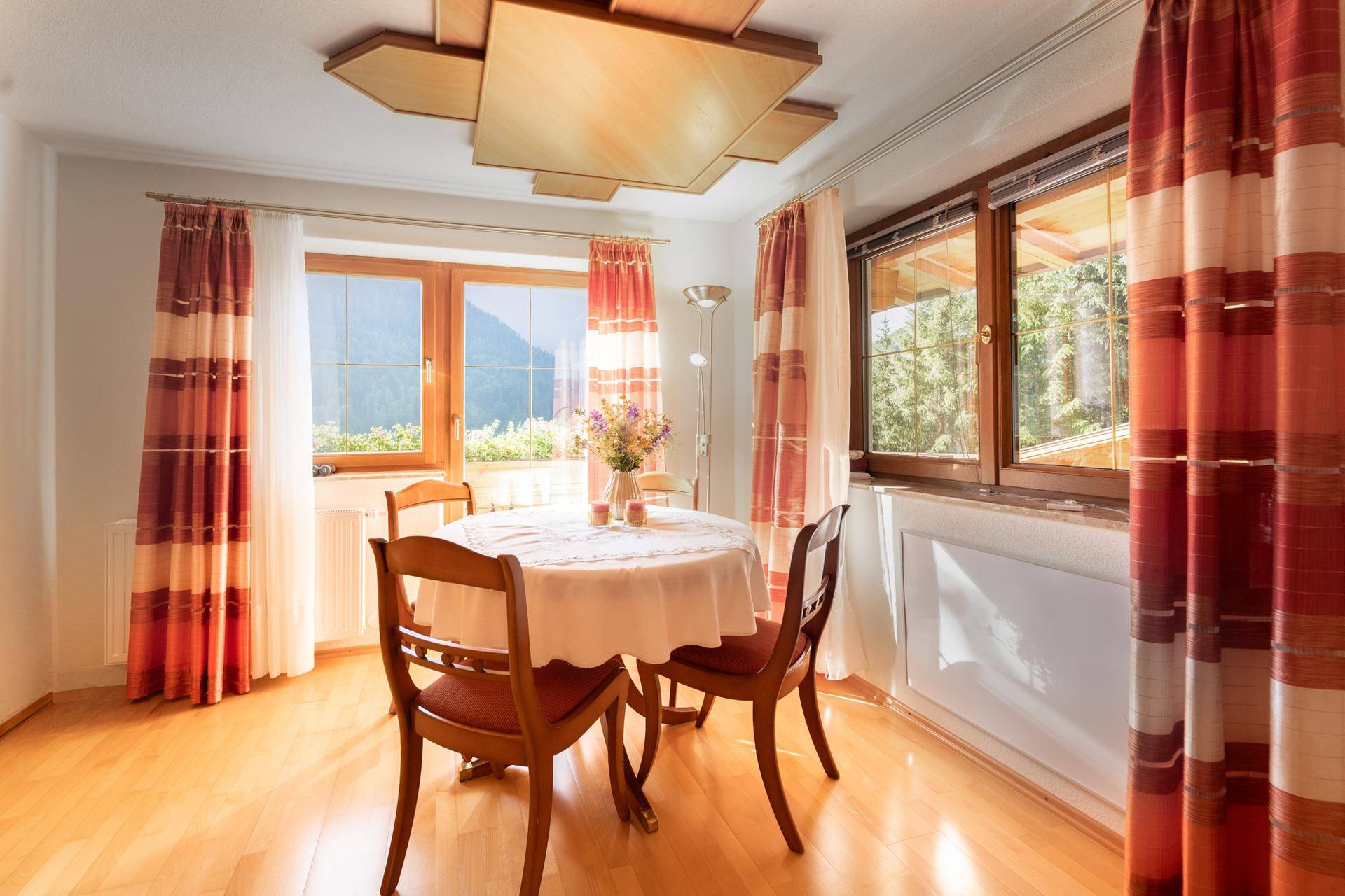 Heller Essbereich mit Holztisch, Stühlen und Fenstern mit Blick ins Grüne.