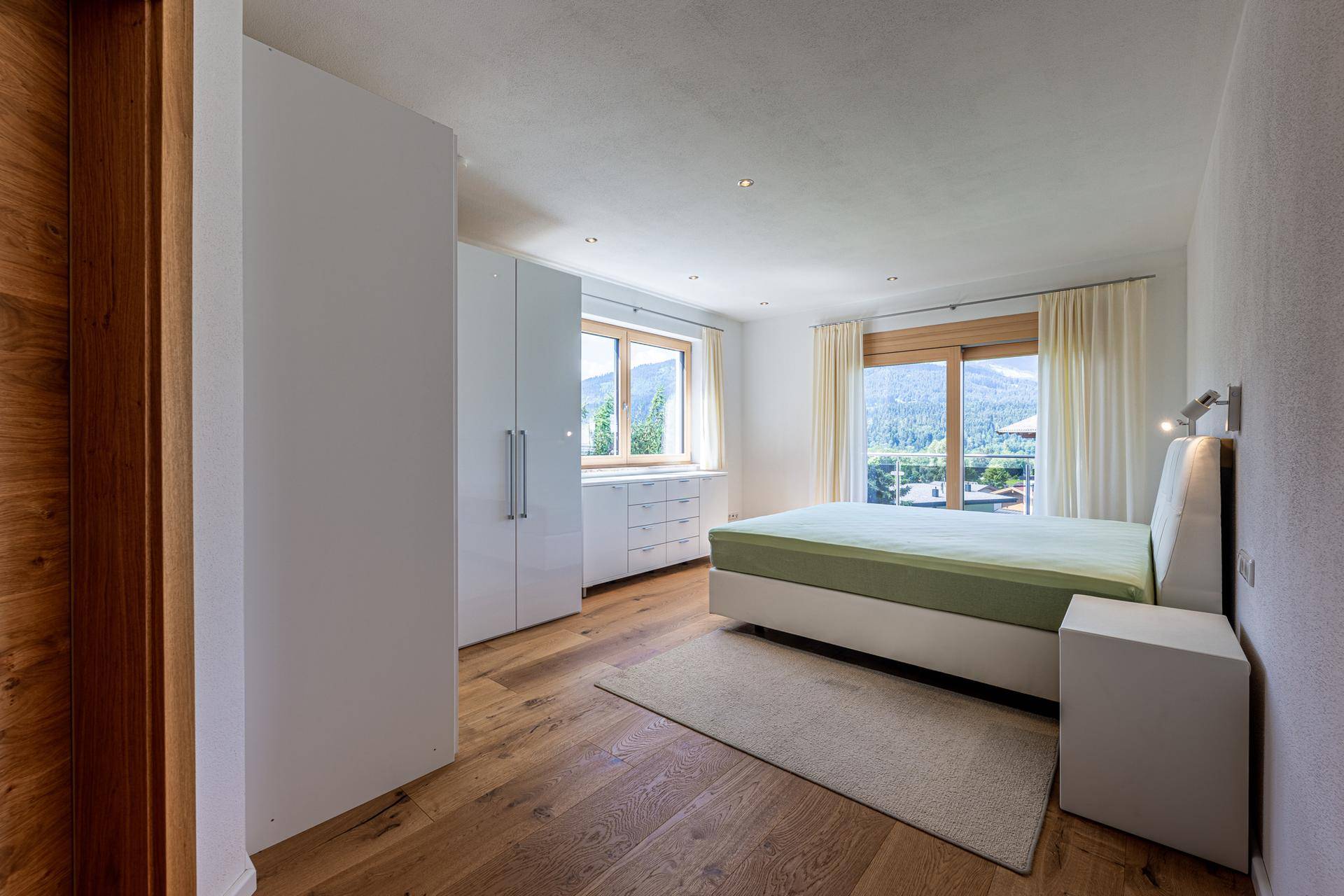 Geräumiges Schlafzimmer mit Holzboden, weißen Schränken und Bergblick aus dem Fenster.