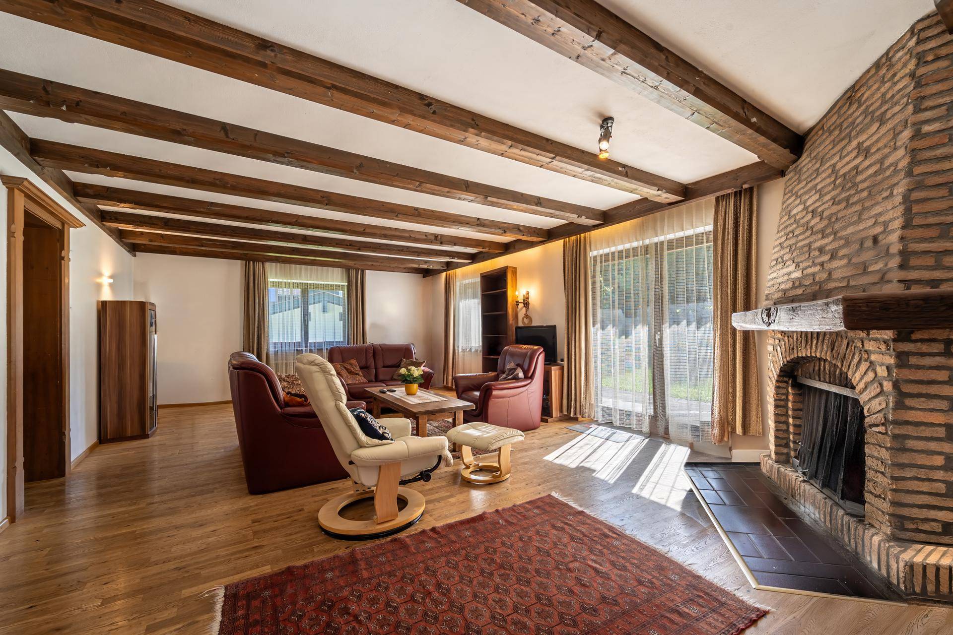 Geräumiges Wohnzimmer mit großem Ziegelkamin, Holzbalkendecke und Zugang zum Garten.