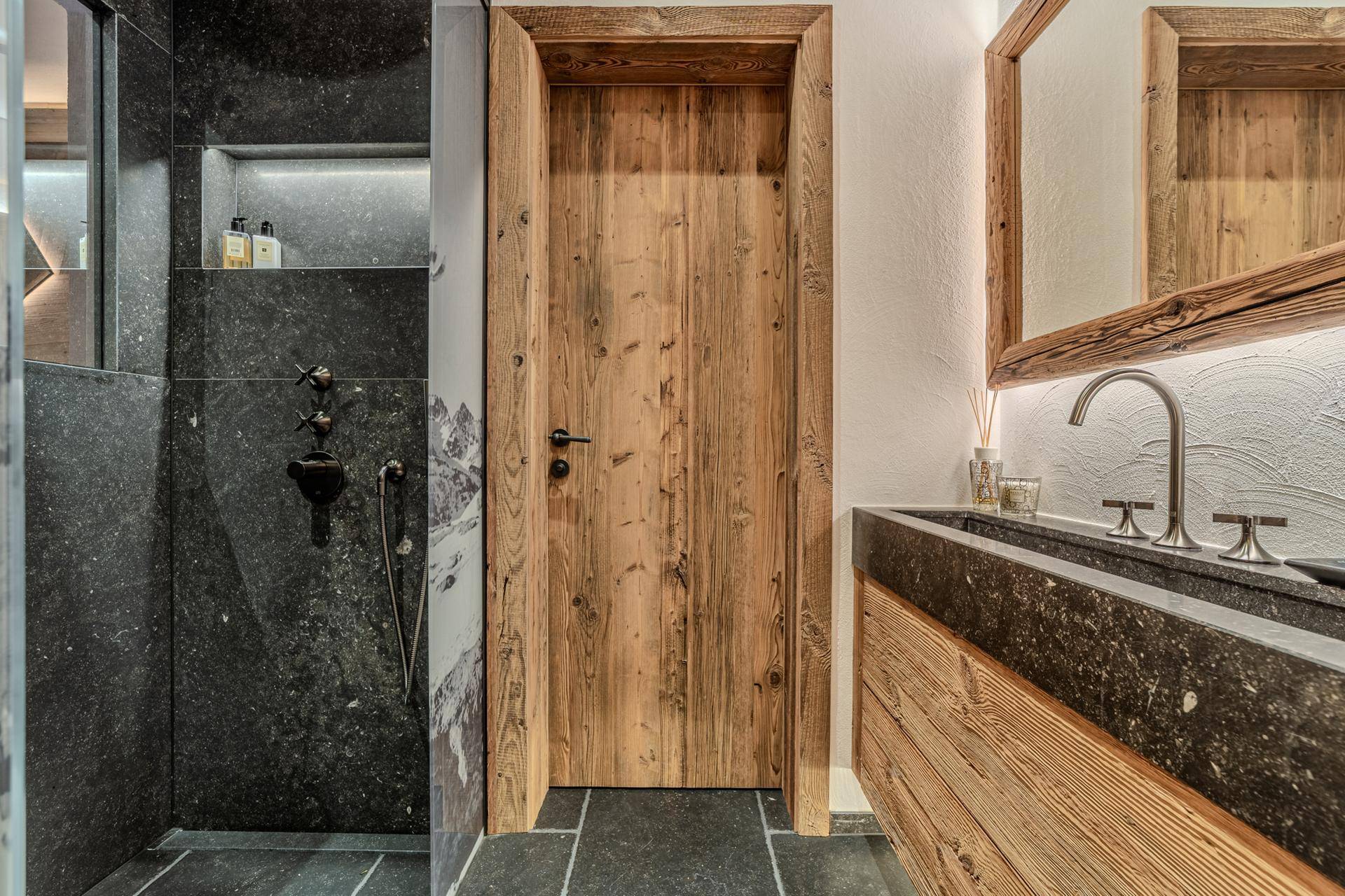 Modernes Badezimmer mit begehbarer Dusche, Steinwaschbecken und Holztür.