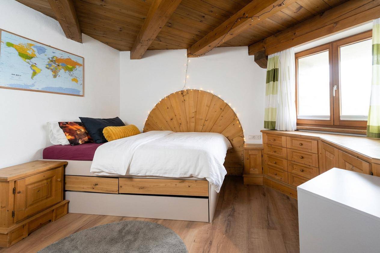 Helles Schlafzimmer mit Holzbett, Stauraum und Blick auf die Umgebung durch das Fenster.