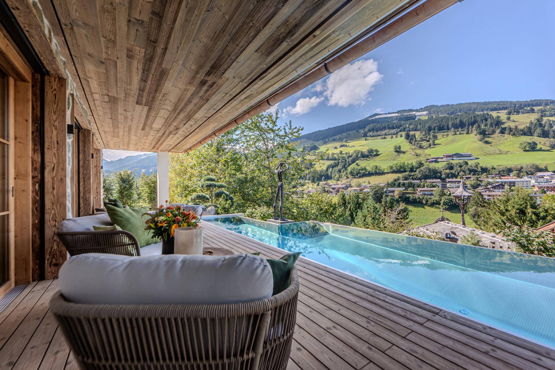 Gemütliche Holzterrasse mit Sitzgelegenheiten und einem Infinity-Pool, der einen weiten Bergblick bietet.