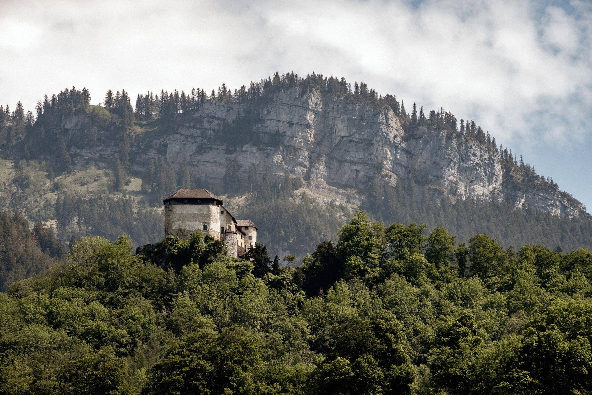 Historisches Gebäude eingebettet in eine bewaldete Berglandschaft unter bewölktem Himmel.