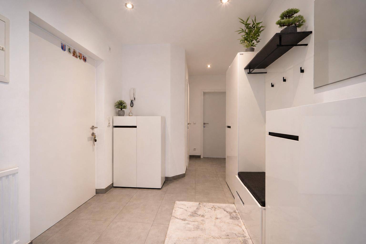 Heller Eingangsbereich mit modernen weißen Möbeln, Fliesenboden und Garderobe.