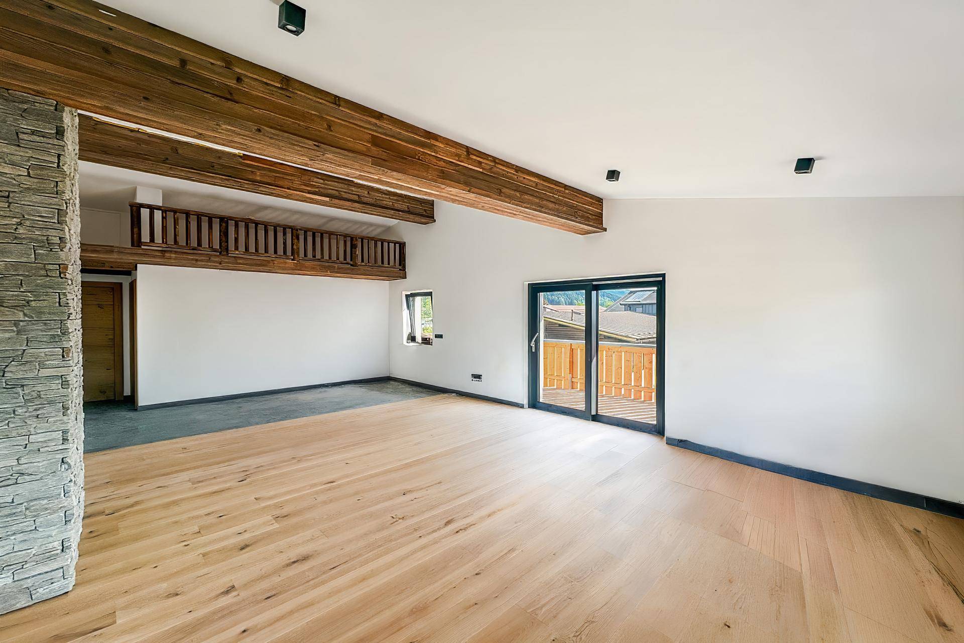 Heller, unmöblierter Wohnbereich mit Holzbalken, Steinwand und Zugang zu einem Balkon.