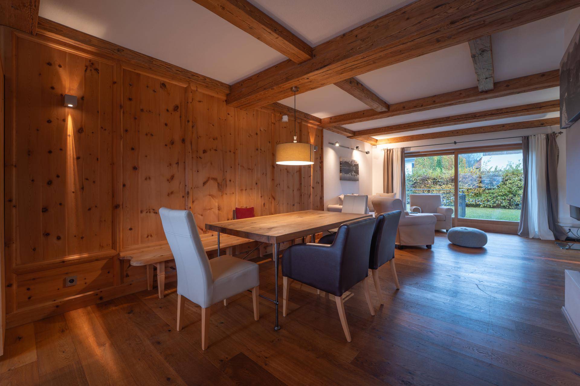 Offener Wohn- und Essbereich mit Holzwänden, Holzbalken und Zugang zum Garten.