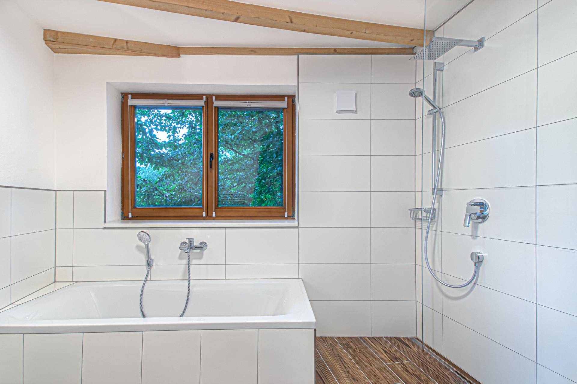 Helles Badezimmer mit Badewanne, Dusche, weißen Fliesen und Holzbalken.