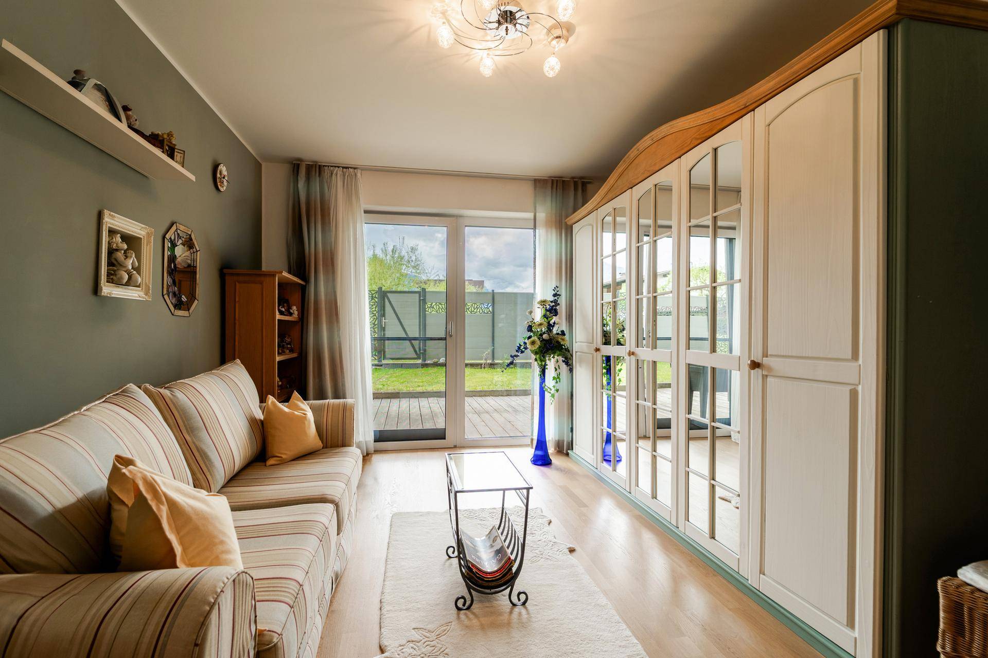 Helles Zimmer mit gestreiftem Sofa, großem Spiegelschrank und Zugang zum Garten.