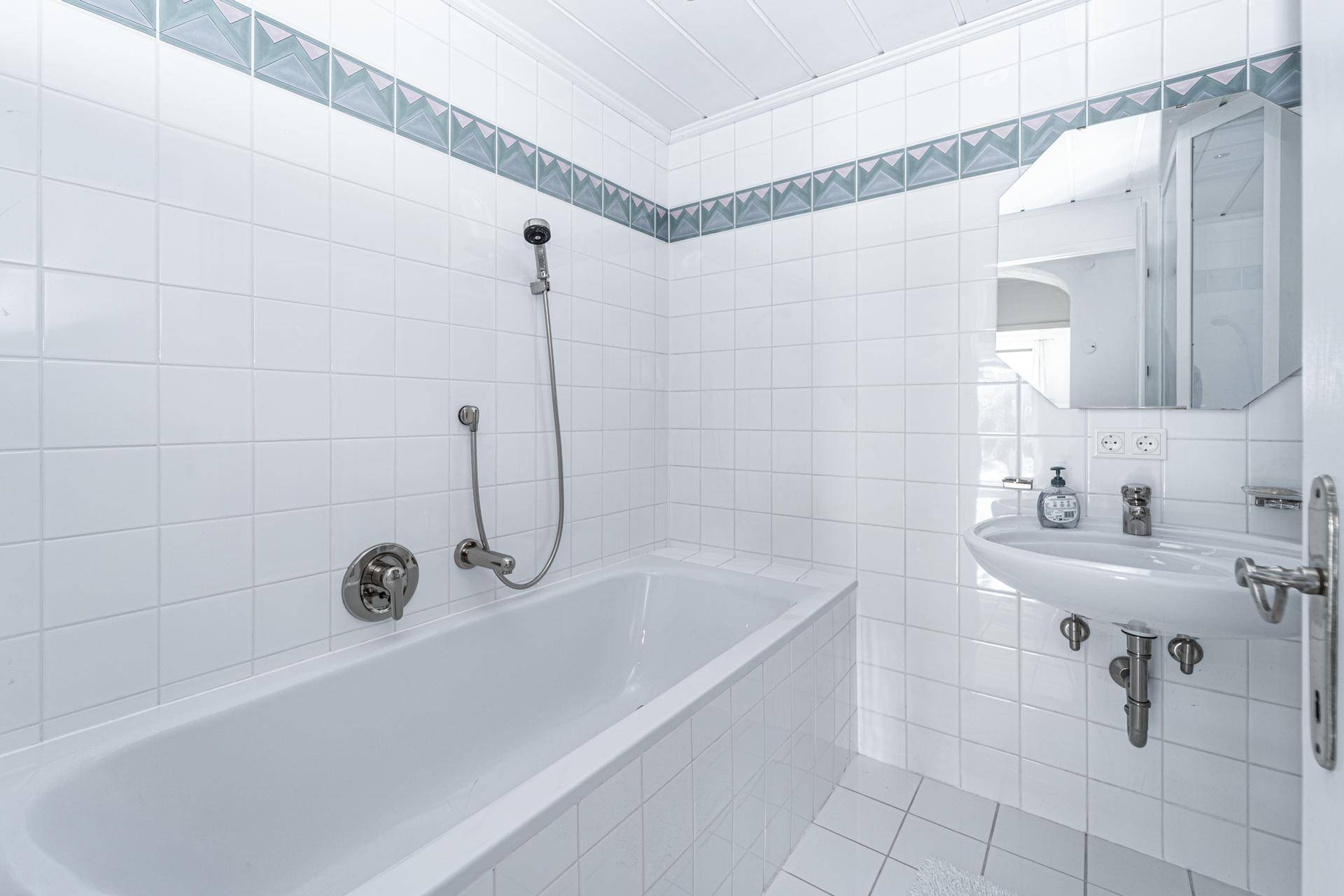 Helles Badezimmer mit Badewanne, Dusche und Waschbecken, komplett gefliest in Weiß.