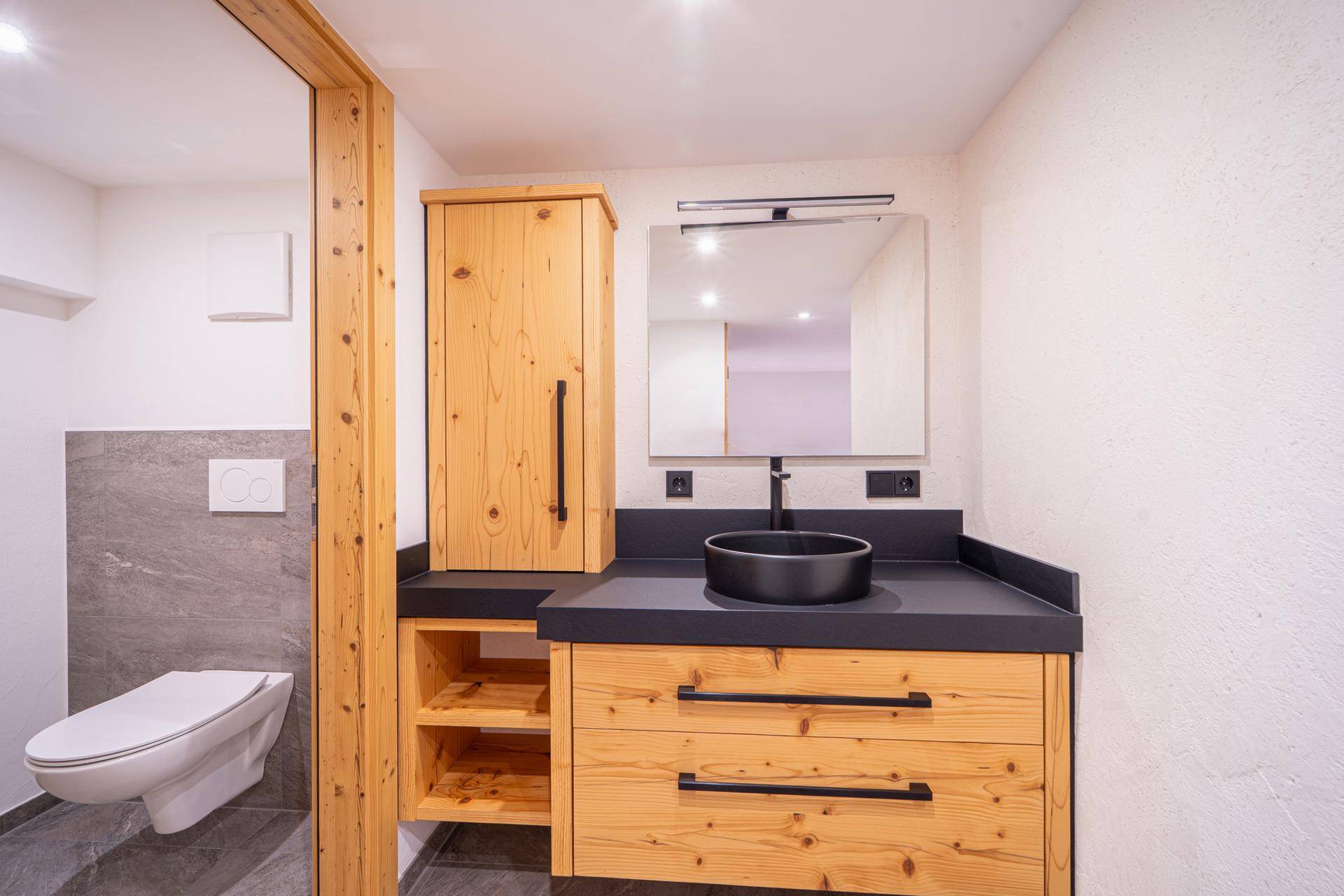 Modernes Gäste-WC mit Waschtisch, Wand-WC und Holzschrank, in hellen und dunklen Kontrasten.