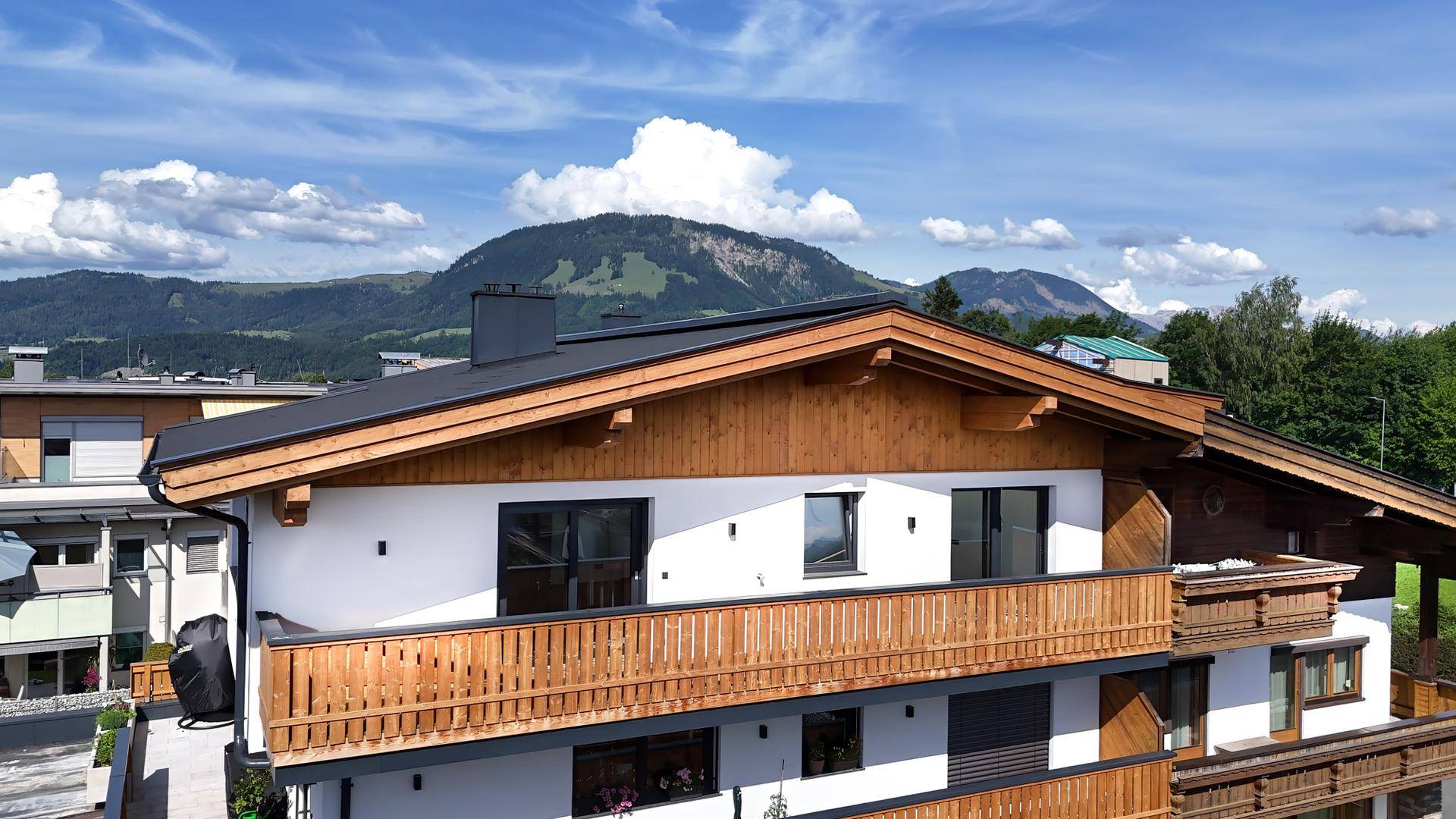 Attraktive Hausfassade mit Holzelementen und einem langen Balkon mit Bergblick.