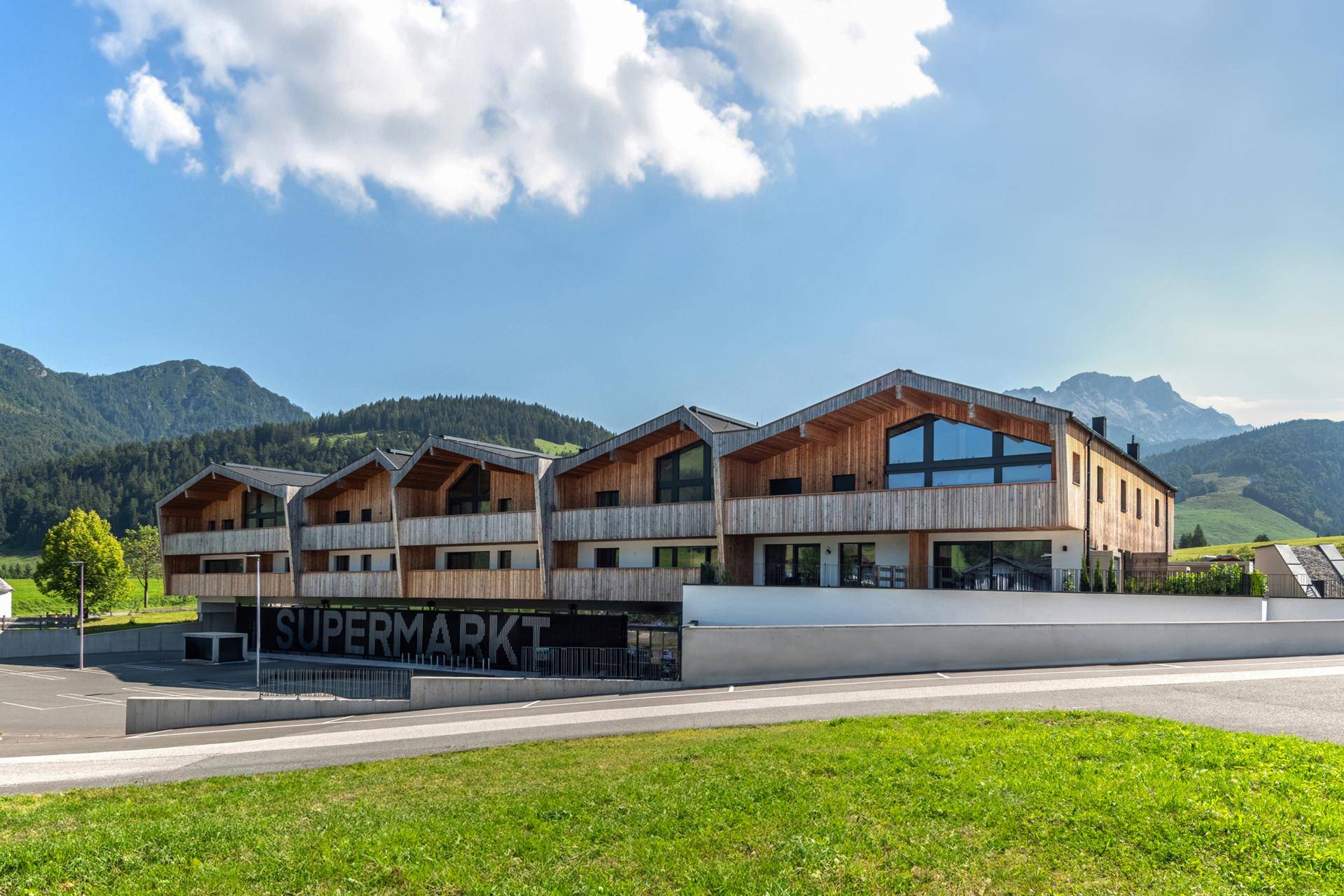 Reihe moderner Holzgebäude mit Satteldächern, integriertem Supermarkt und Bergblick.