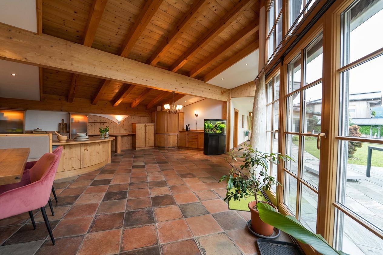 Heller, offener Wohnbereich mit hohen Holzdecken, großen Fenstern und Terrakotta-Fliesenboden.
