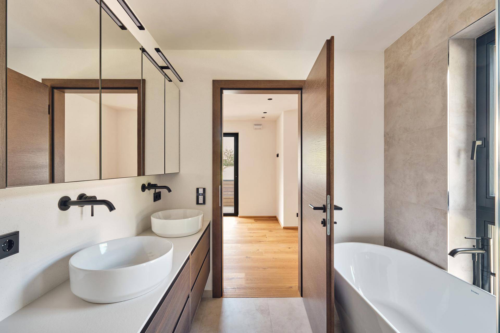 Modernes Badezimmer mit Doppelwaschbecken, Badewanne und dunklen Armaturen.