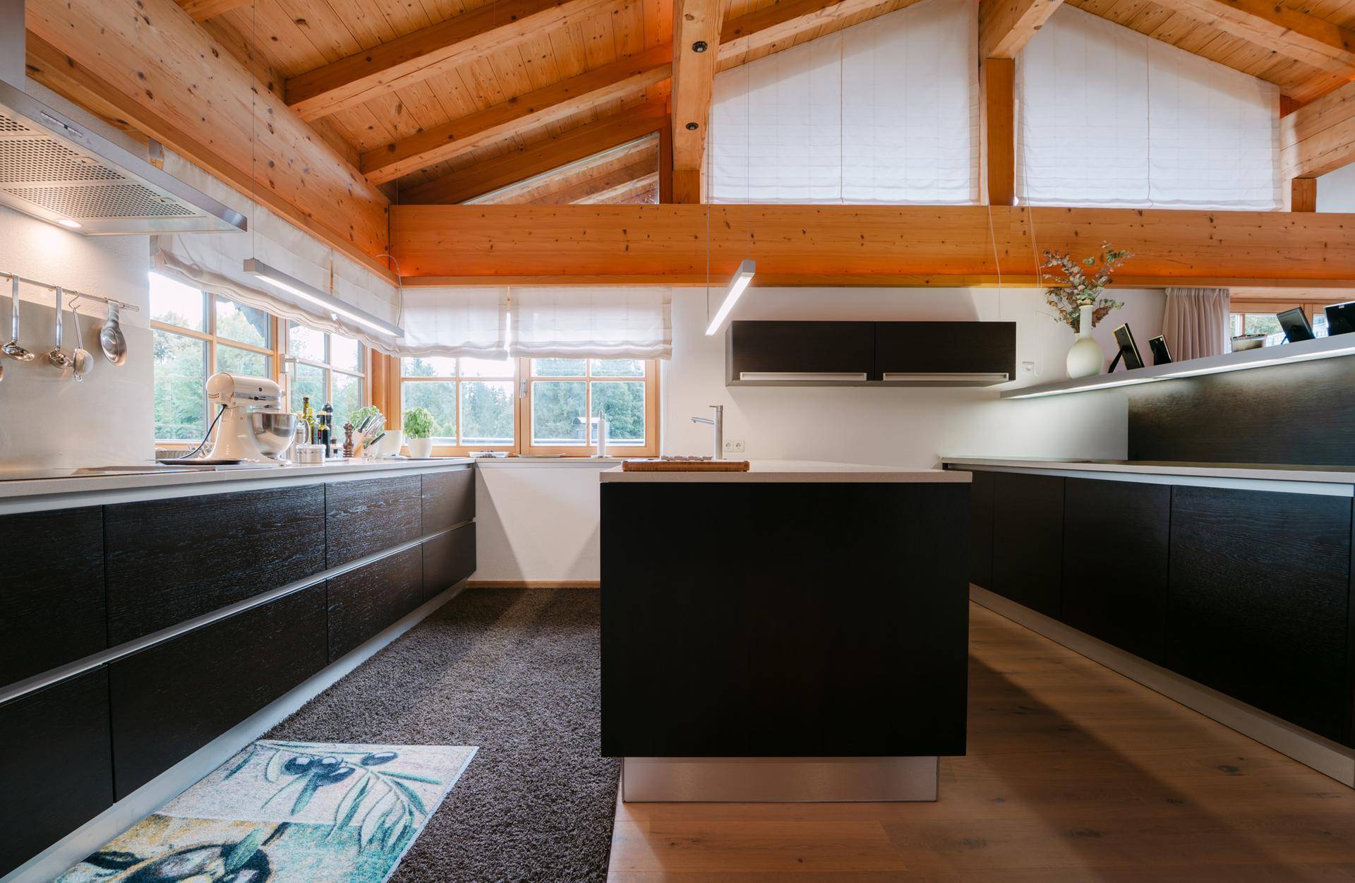 Moderne Küche mit dunklen Schränken, Kücheninsel und Holzbalkendecke, bietet viel Arbeitsfläche.