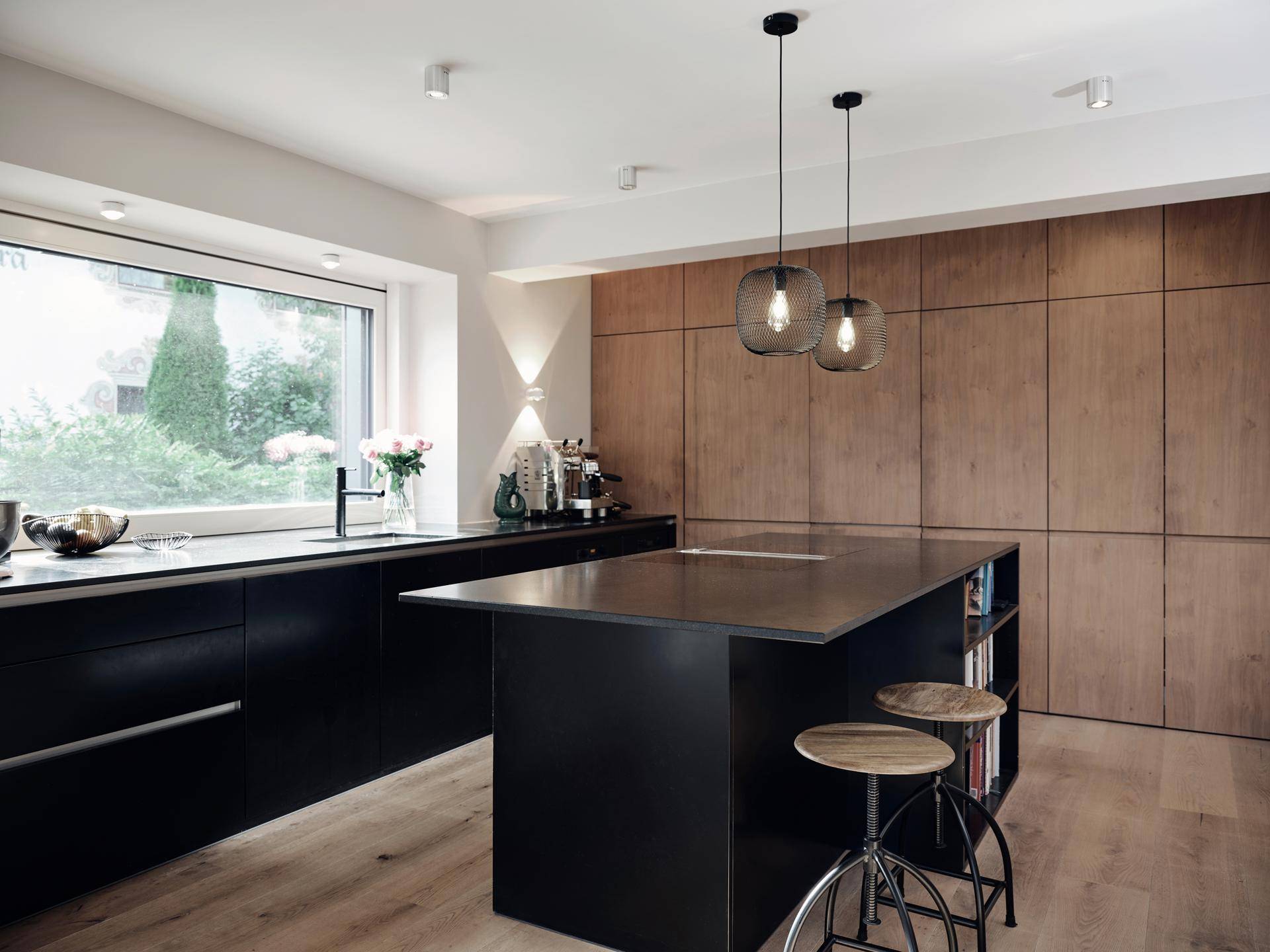Elegante, moderne Küche mit schwarzer Kücheninsel, Holzverkleidung und großem Fenster für viel Tageslicht.