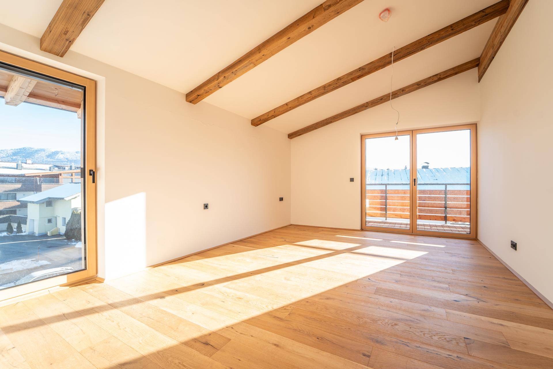 Lichtdurchfluteter Raum mit Holzbalken, Holzboden und Schiebetüren zum Balkon, ideal als Schlafzimmer.