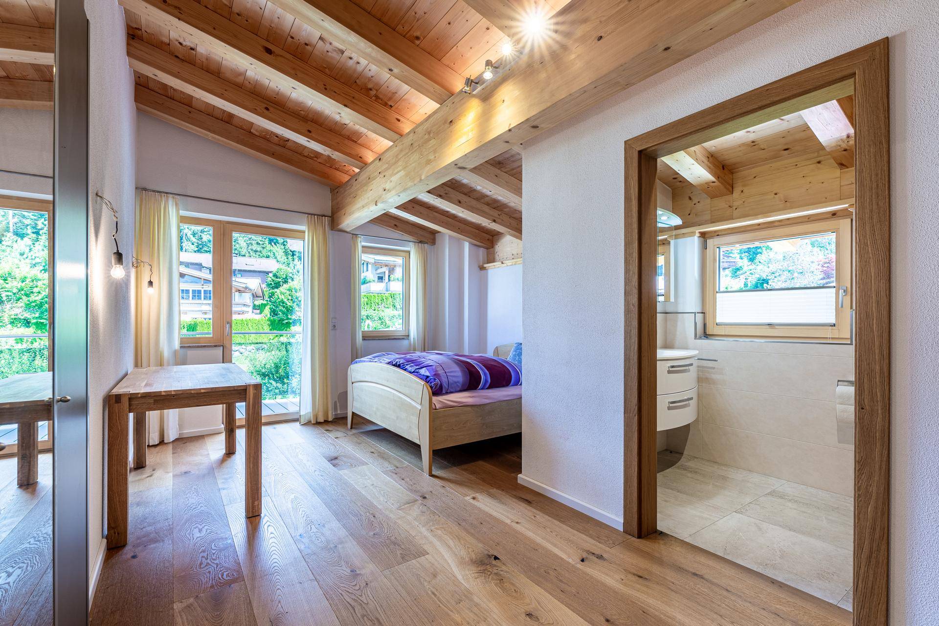 Helles Schlafzimmer mit Holzbalkendecke, Parkettboden und Zugang zu einem Badezimmer.