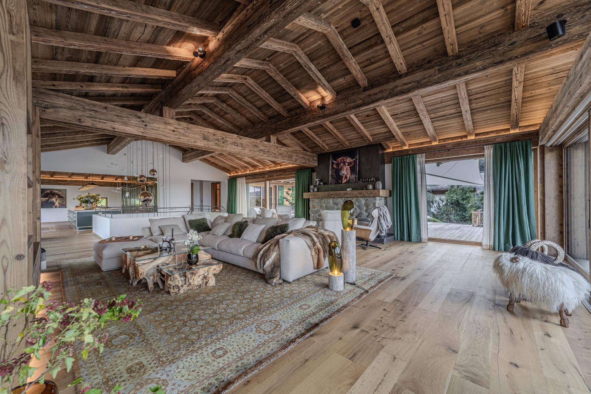 Großzügiges Wohnzimmer im Chalet-Stil mit Holzbalkendecke, gemütlicher Sitzecke und Blick ins Grüne.