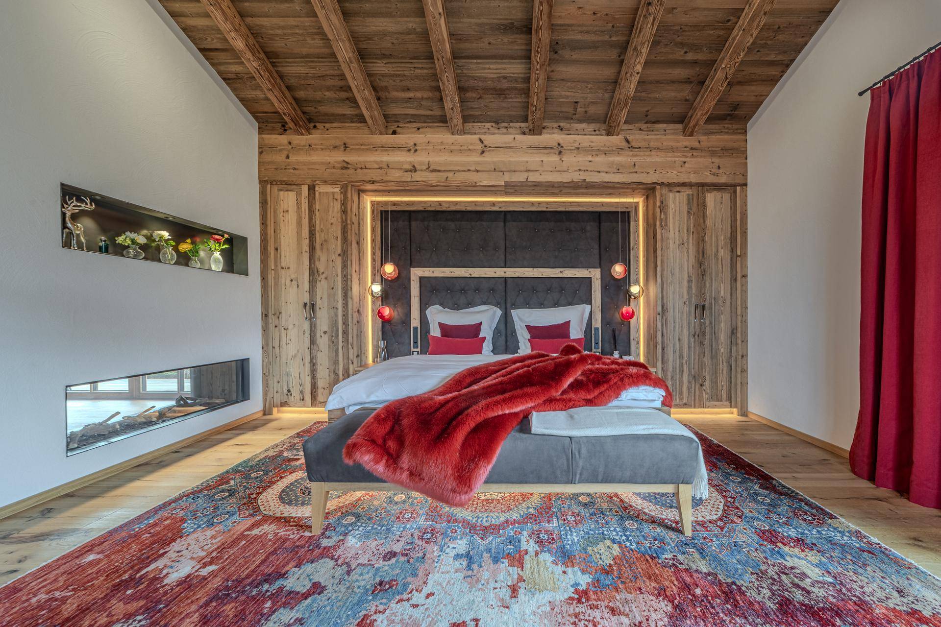 Schlafzimmer im alpinen Stil mit Holzwänden, rotem Teppich und integriertem Kamin.