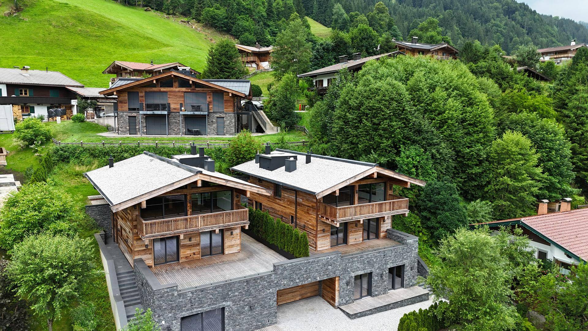 Weitläufige Luftaufnahme der modernen Chalet-Häuser, eingebettet in die üppigen grünen Hügel.