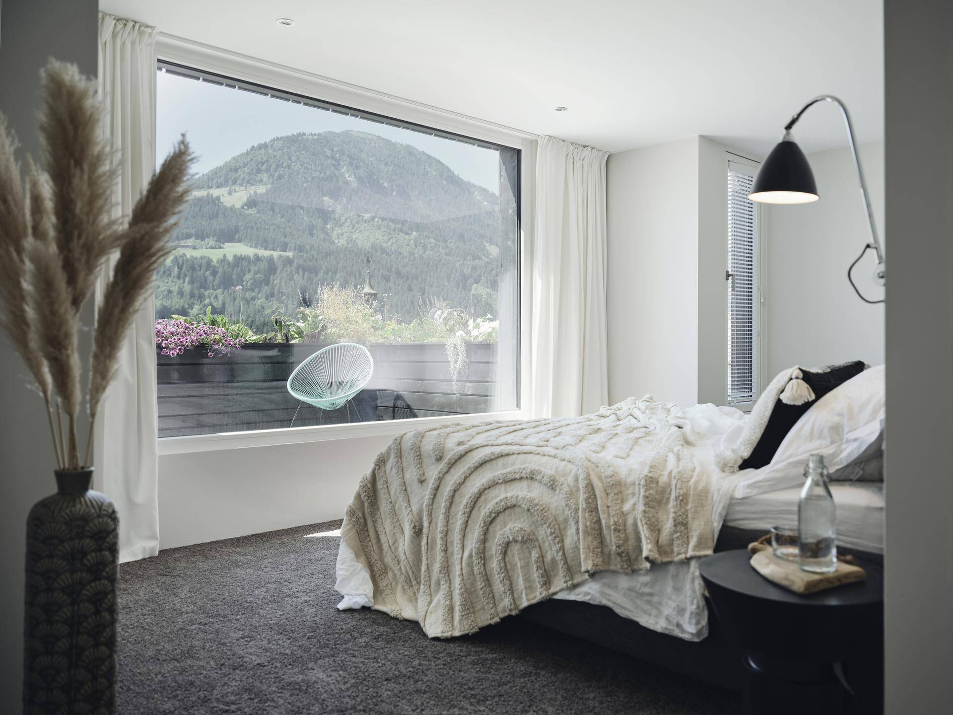 Helles Schlafzimmer mit großem Fenster, das einen weiten Blick auf die umliegende Berglandschaft ermöglicht.