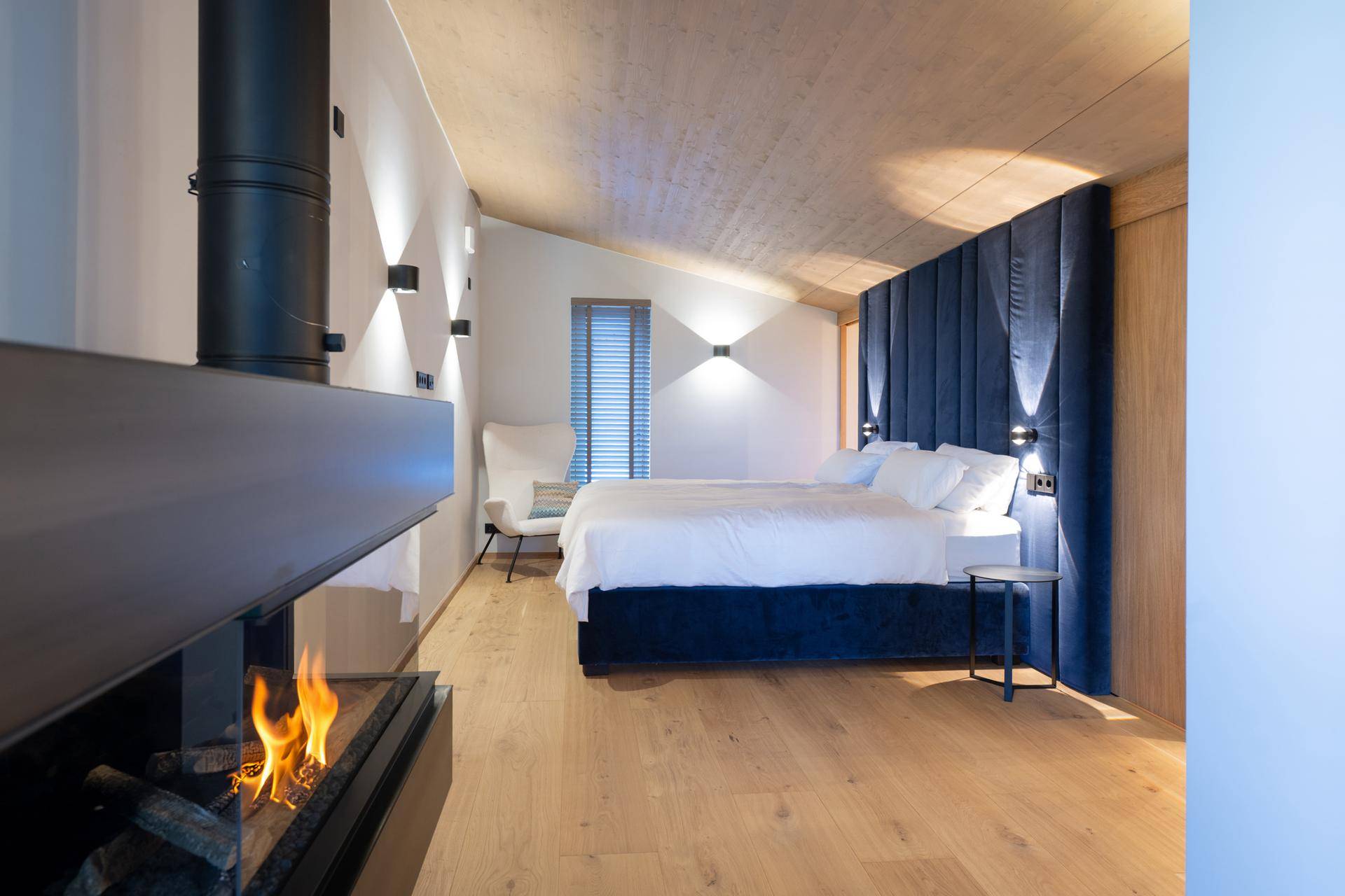 Schlafzimmer mit Holzboden, modernem Kamin und blauer Akzentwand unter Dachschräge.