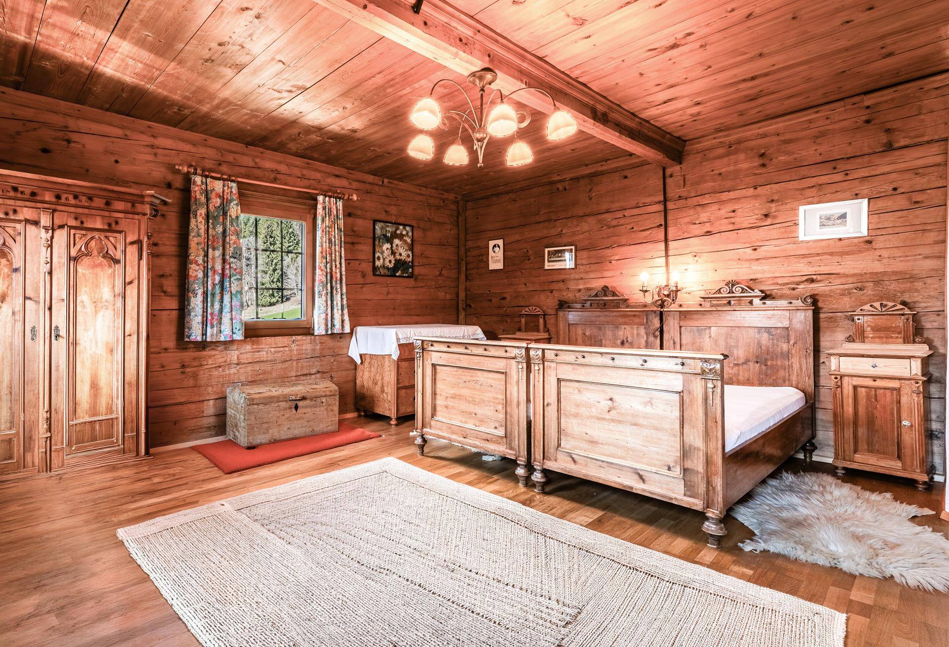 Rustikales Schlafzimmer mit Holztäfelung, traditionellem Bett, Holzboden und Blick ins Grüne.