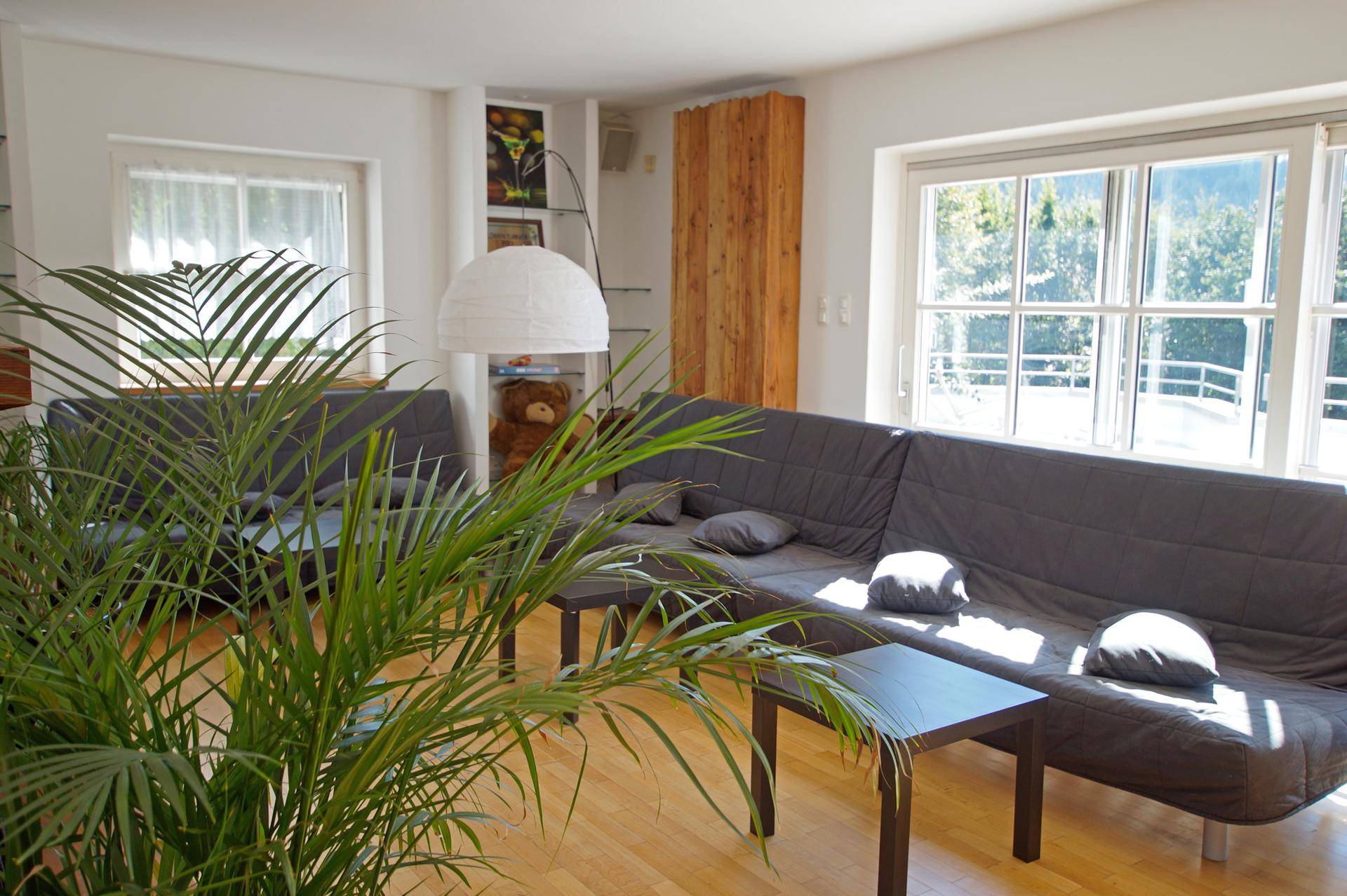 Gemütlicher Wohnbereich mit großem Sofa, Holzboden und Blick ins Grüne durch die Fenster.