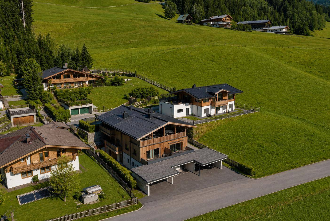 Luftaufnahme einer Gruppe von Chalet-Häusern eingebettet in eine grüne Berglandschaft.