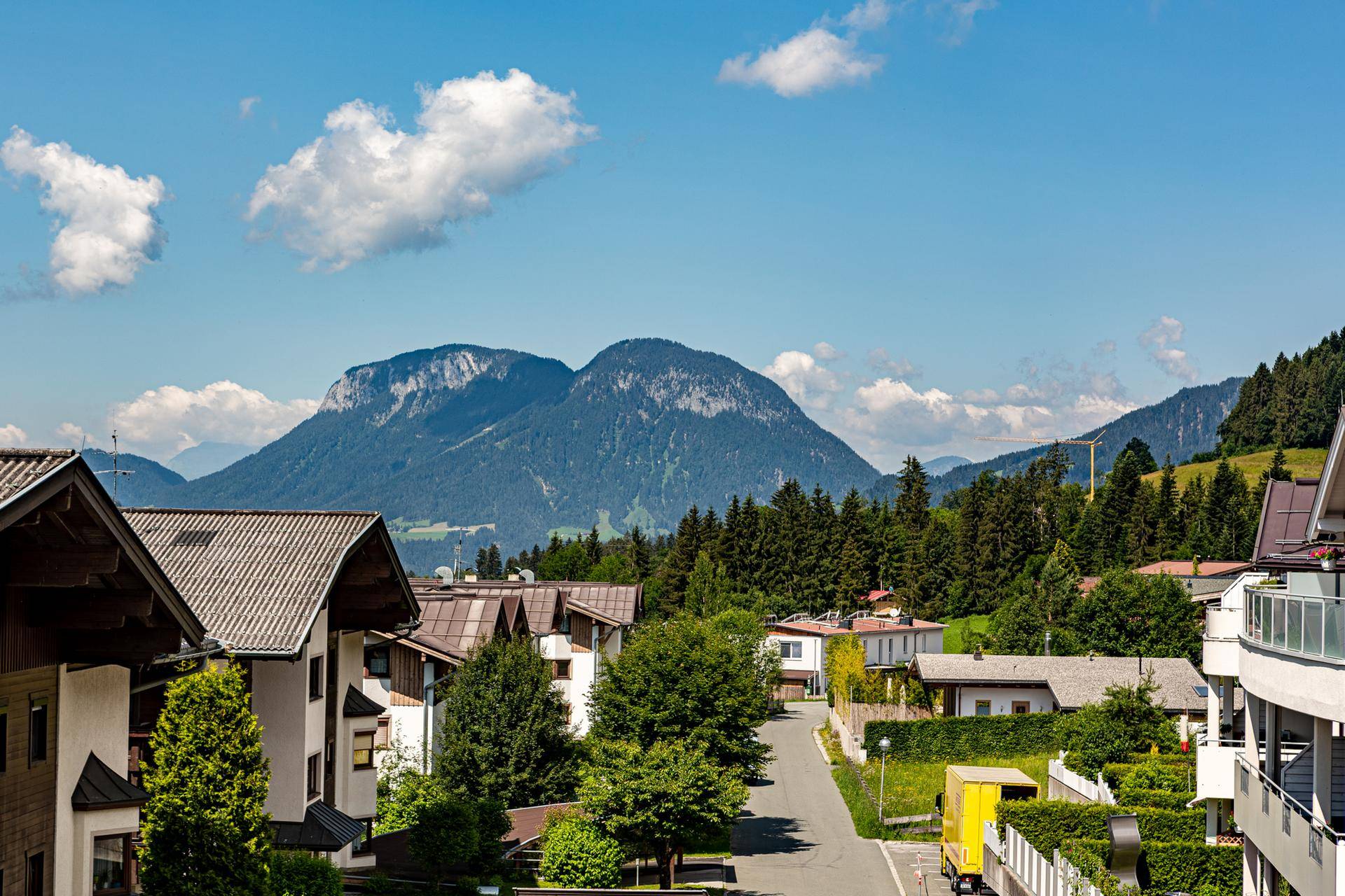 Panoramablick auf eine Berglandschaft mit Häusern und einer Straße unter blauem Himmel.