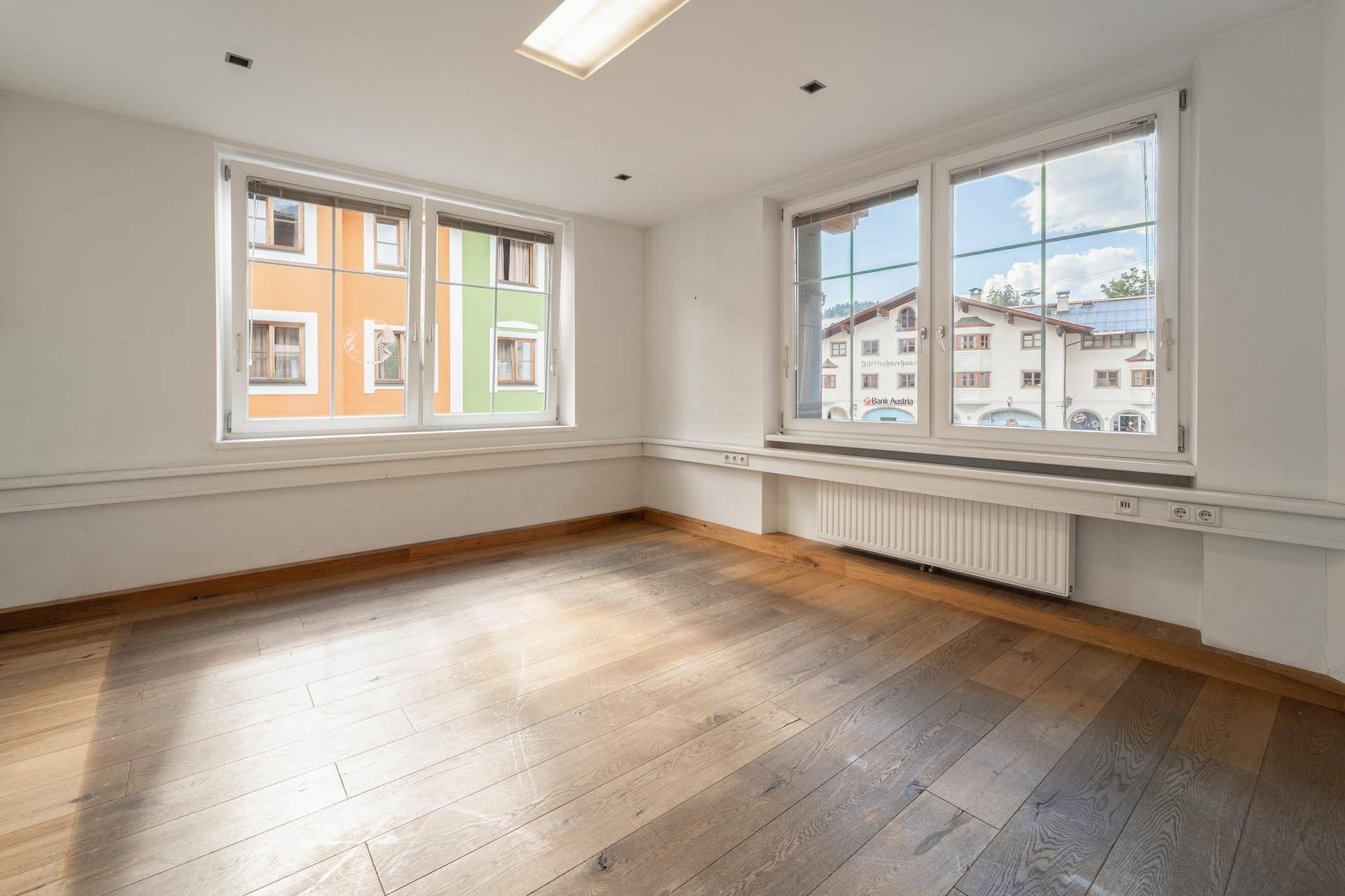 Geräumiges Büro mit Holzboden und mehreren Fenstern, die auf die Stadt blicken.