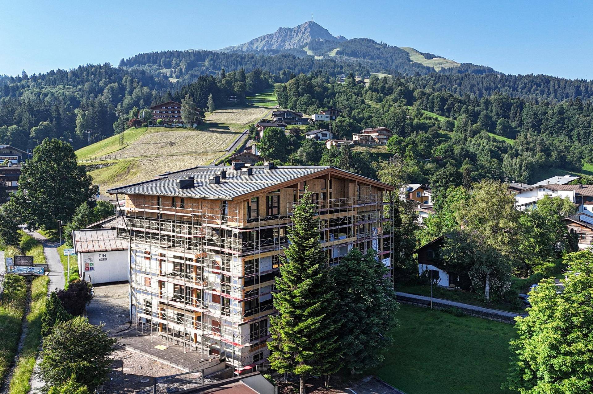 Luftaufnahme eines im Bau befindlichen Gebäudes mit Gerüst, eingebettet in eine grüne Berglandschaft.